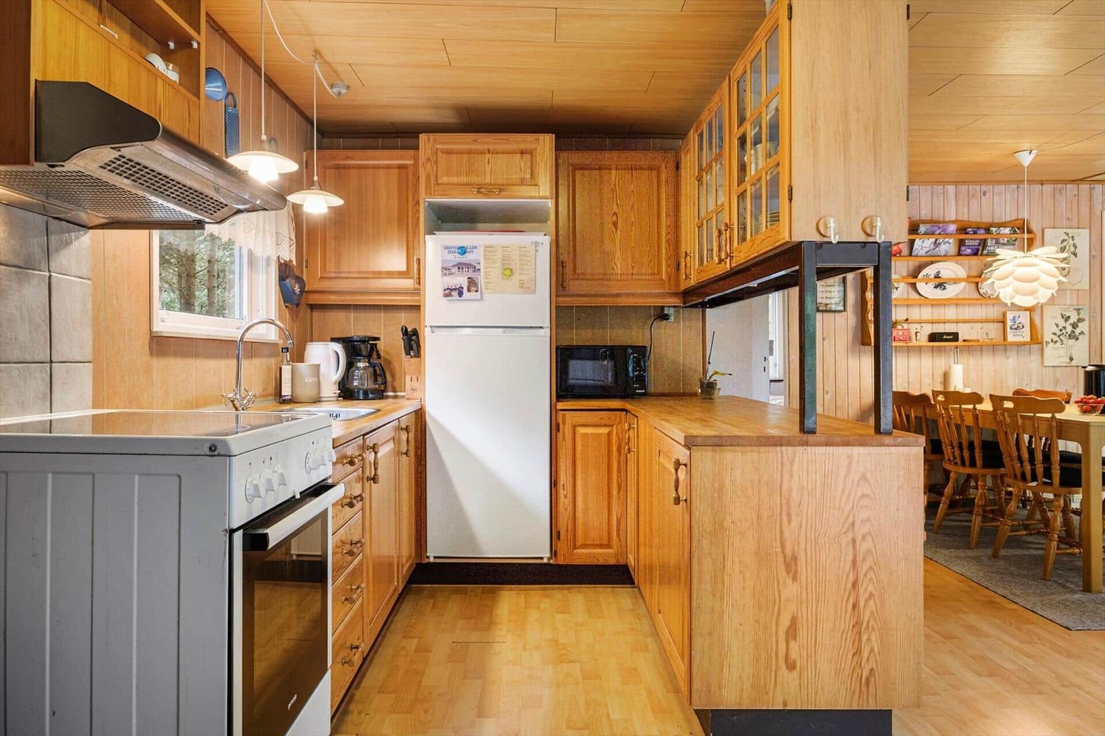 Wooden kitchen with white cooker, refrigerator, microwave and view into the dining area.
