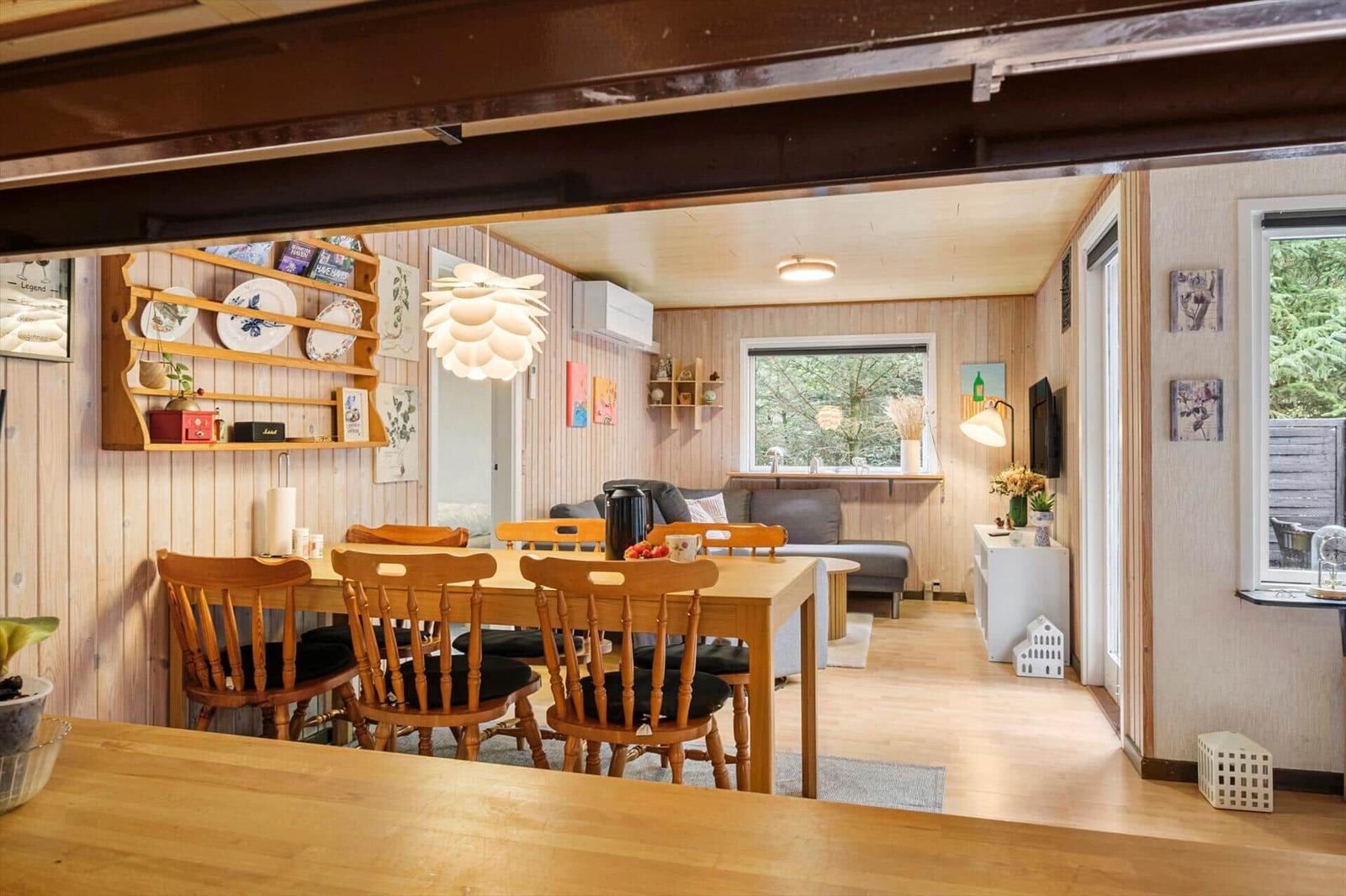 Open living dining area with wooden table, six chairs, grey sofa and a television.