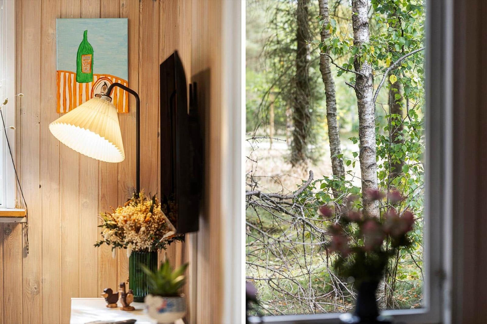Wall lamp with pleated shade next to dried flowers and forest view through a window.