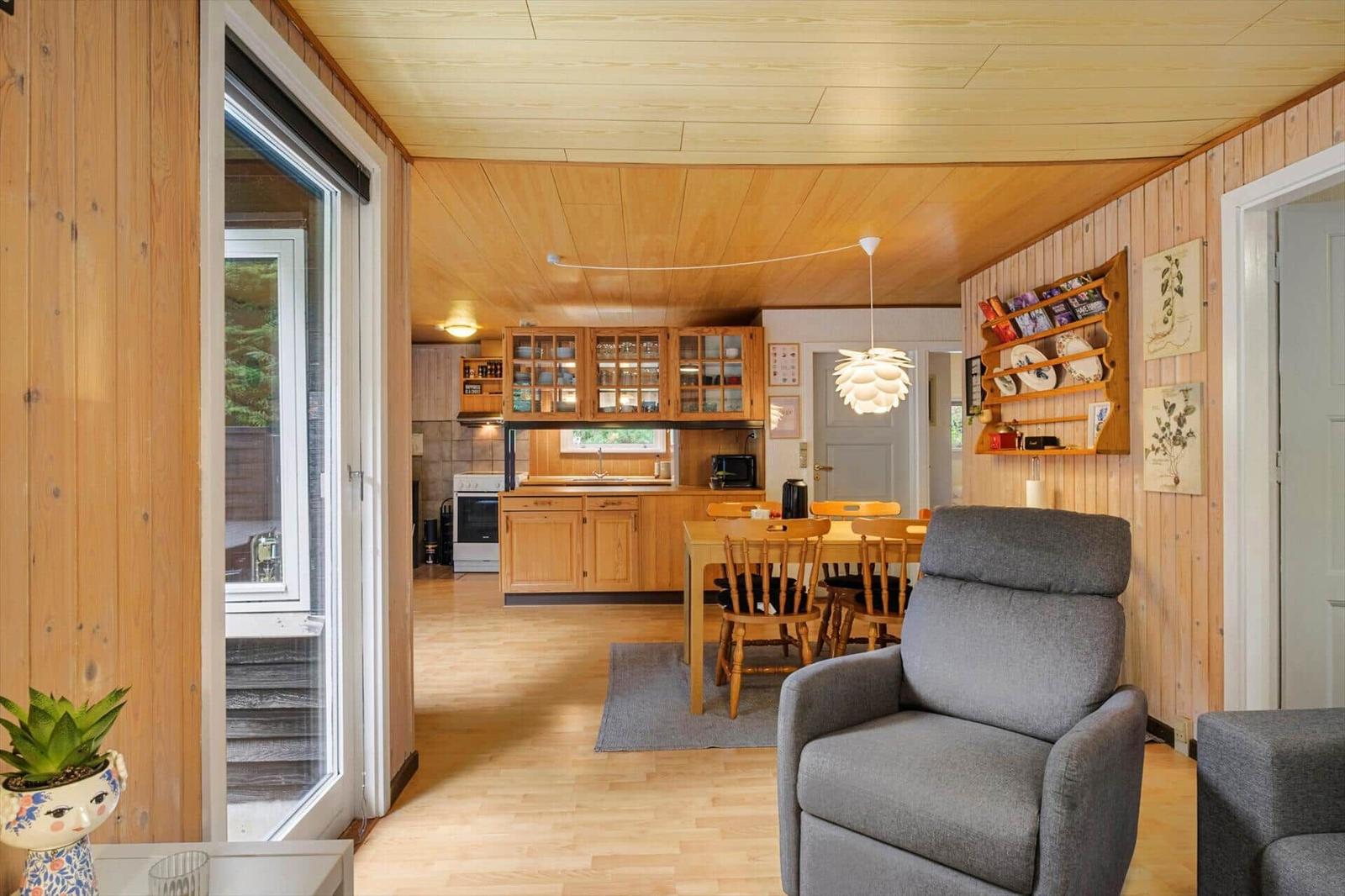 Open living space with dining table, pinecone lamp, grey armchair and kitchen in the background.