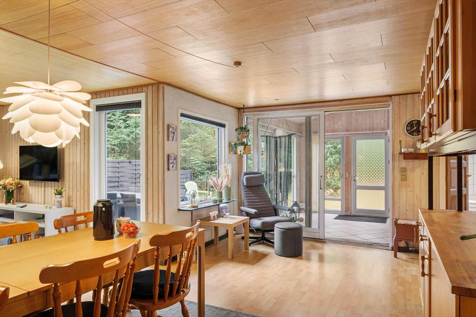 Open living dining area with wooden table, grey recliner and glass doors to a sunroom.