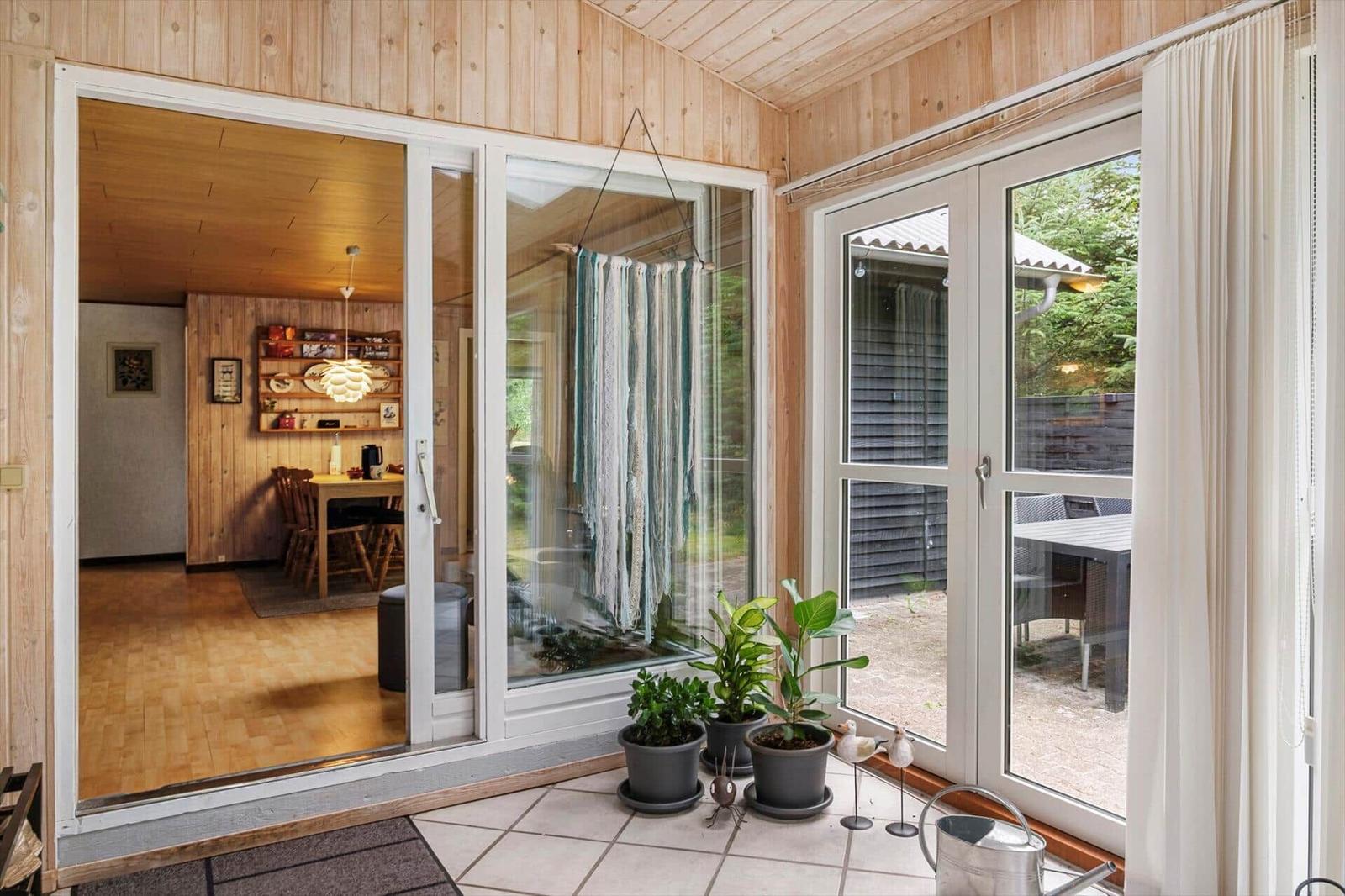 Bright hallway with wood paneling, indoor plants and glass doors to terrace and living area.