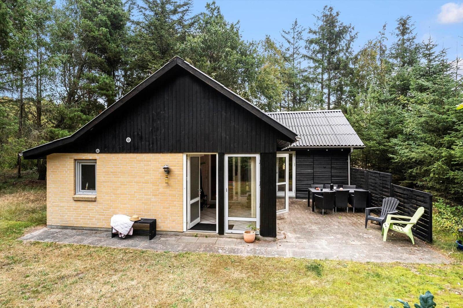 House with yellow brick wall, black wood siding, terrace, dining table and lounge chairs.