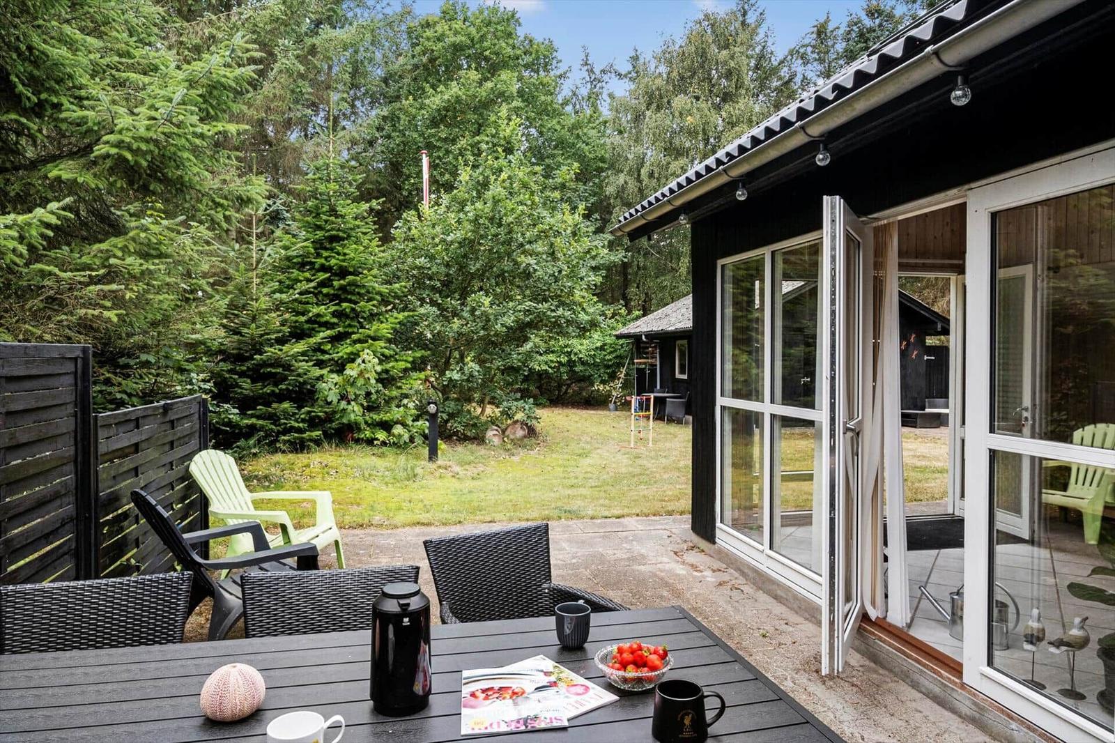 Terrace with dark dining table, wicker chairs and black wooden house by the garden.