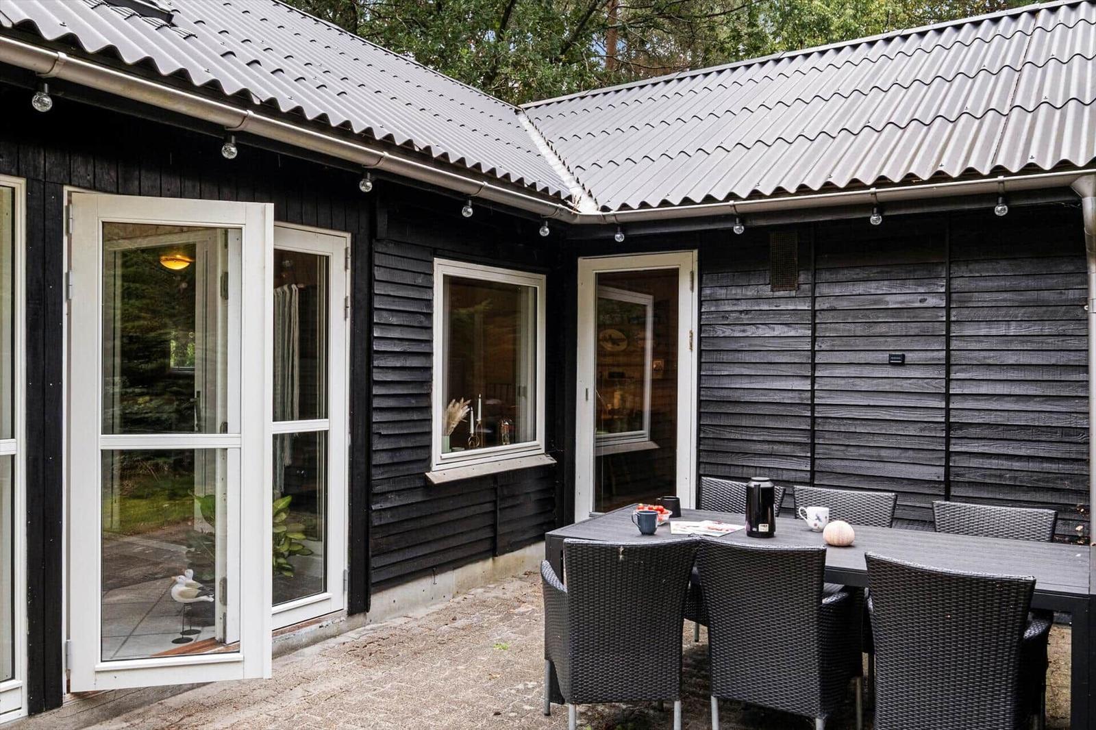 Terrace with black dining table and wicker chairs by a dark wooden house.