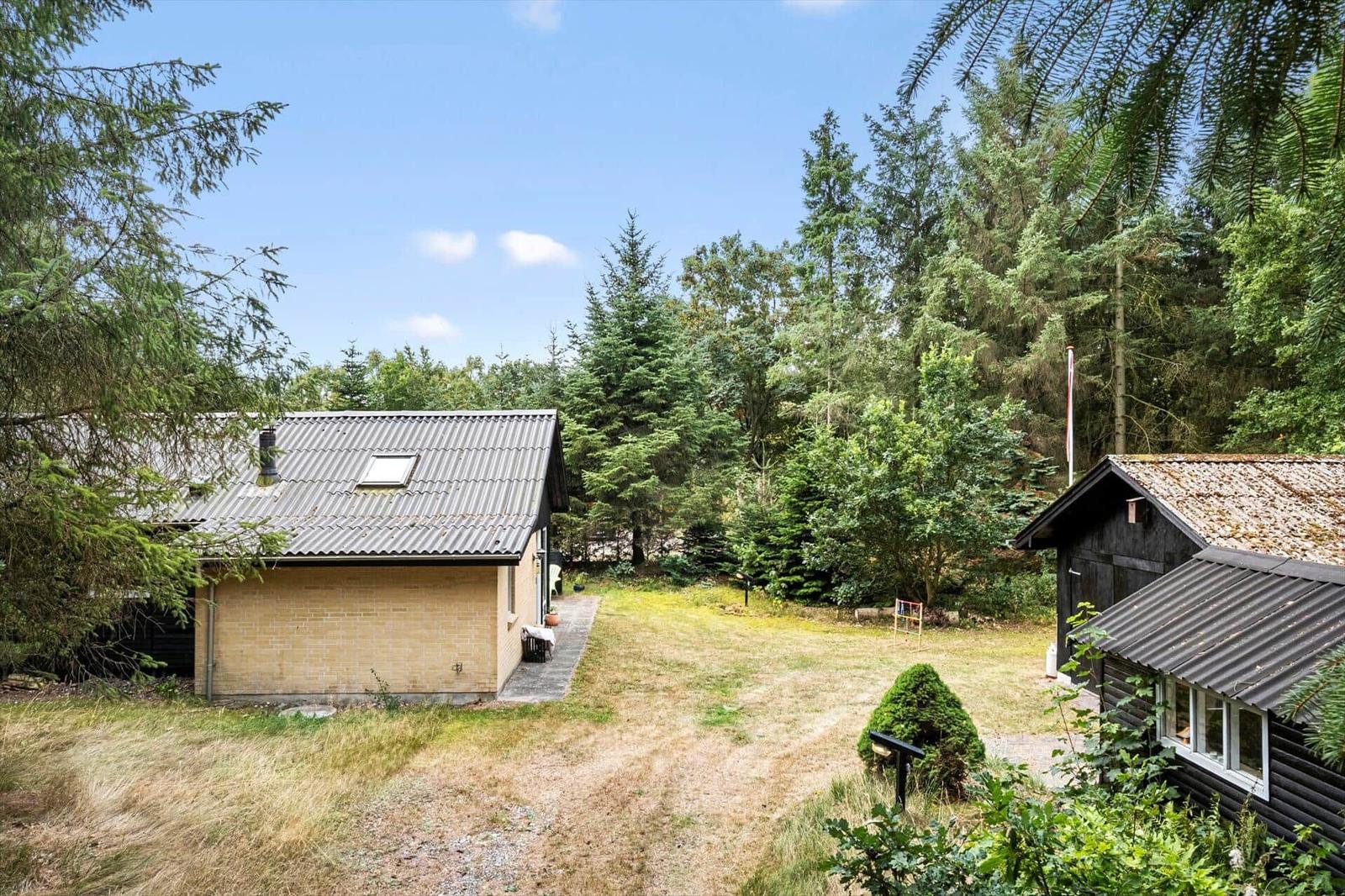 Yellow brick house and dark outbuilding on a lawn surrounded by forest.