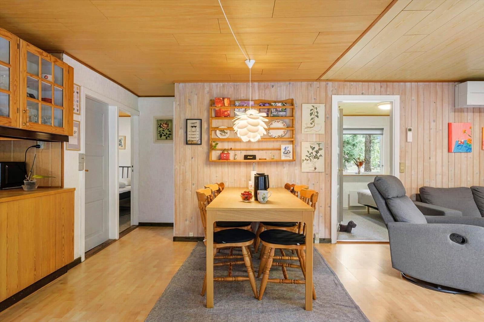 Open living dining area with wooden table, six chairs, pinecone lamp and grey armchair.