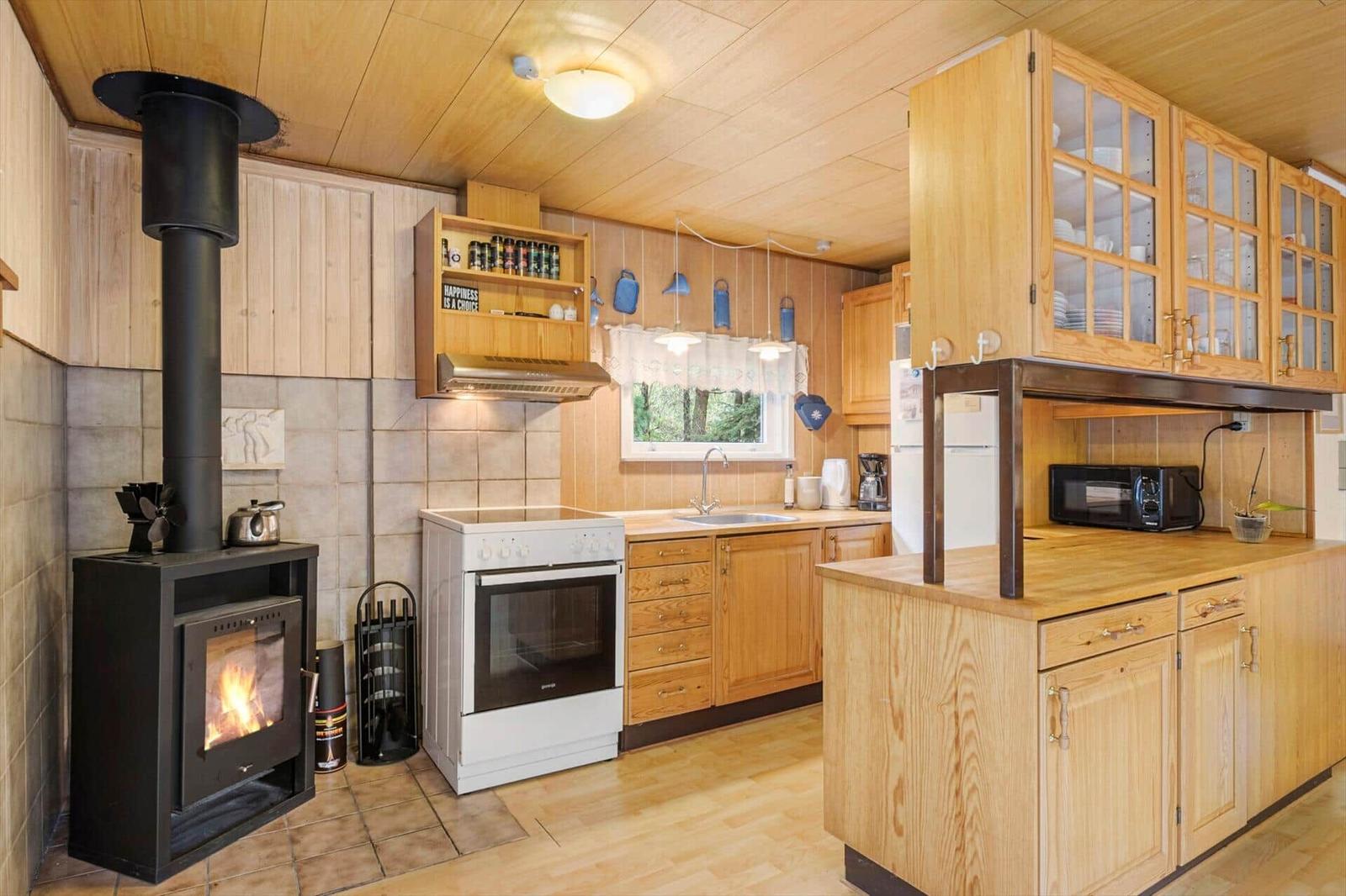 Wooden kitchen with wood stove, white cooker, sink at the window and microwave on the counter.