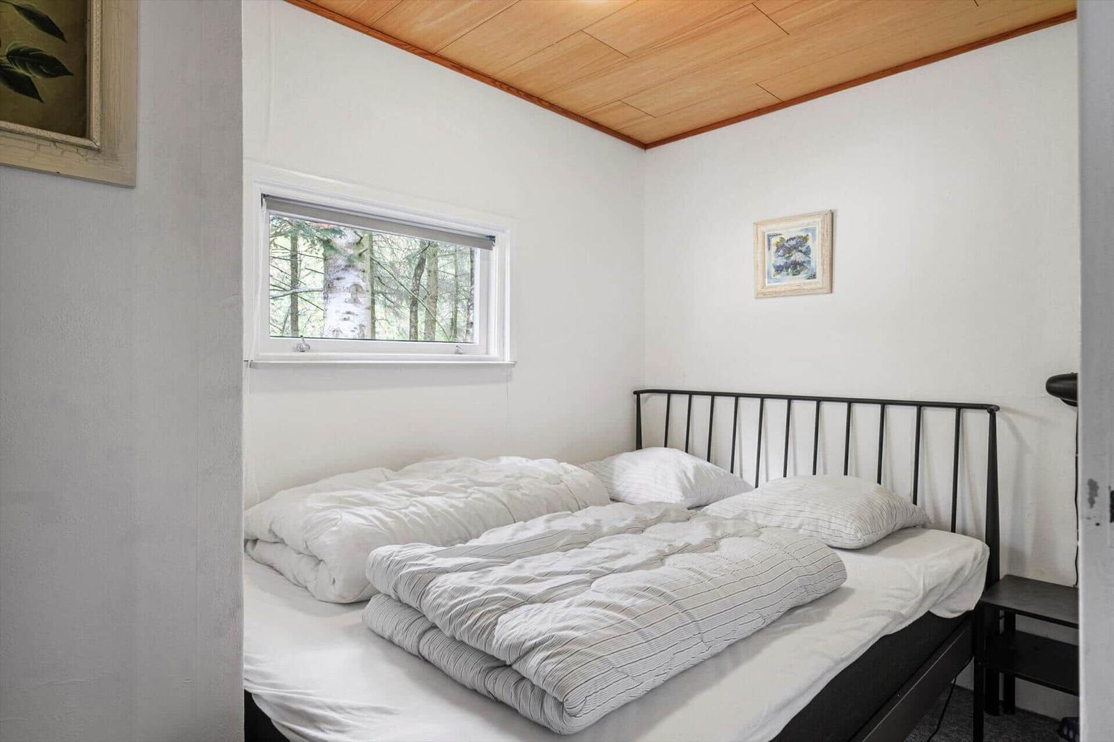 Bedroom with double bed, metal frame, wood ceiling and window with forest view.