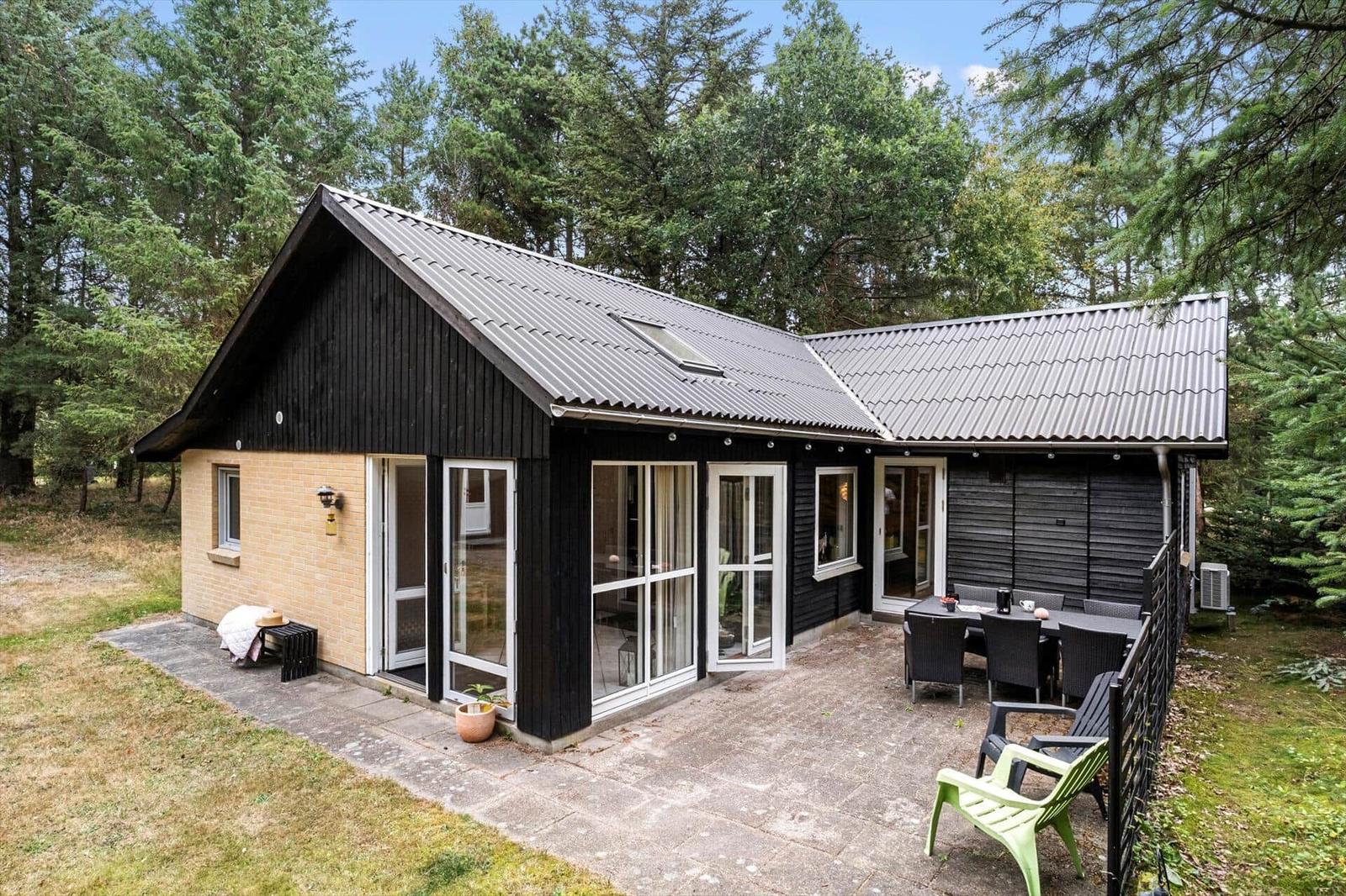 Black wooden house with yellow brick, terrace, garden furniture and large windows in the forest.