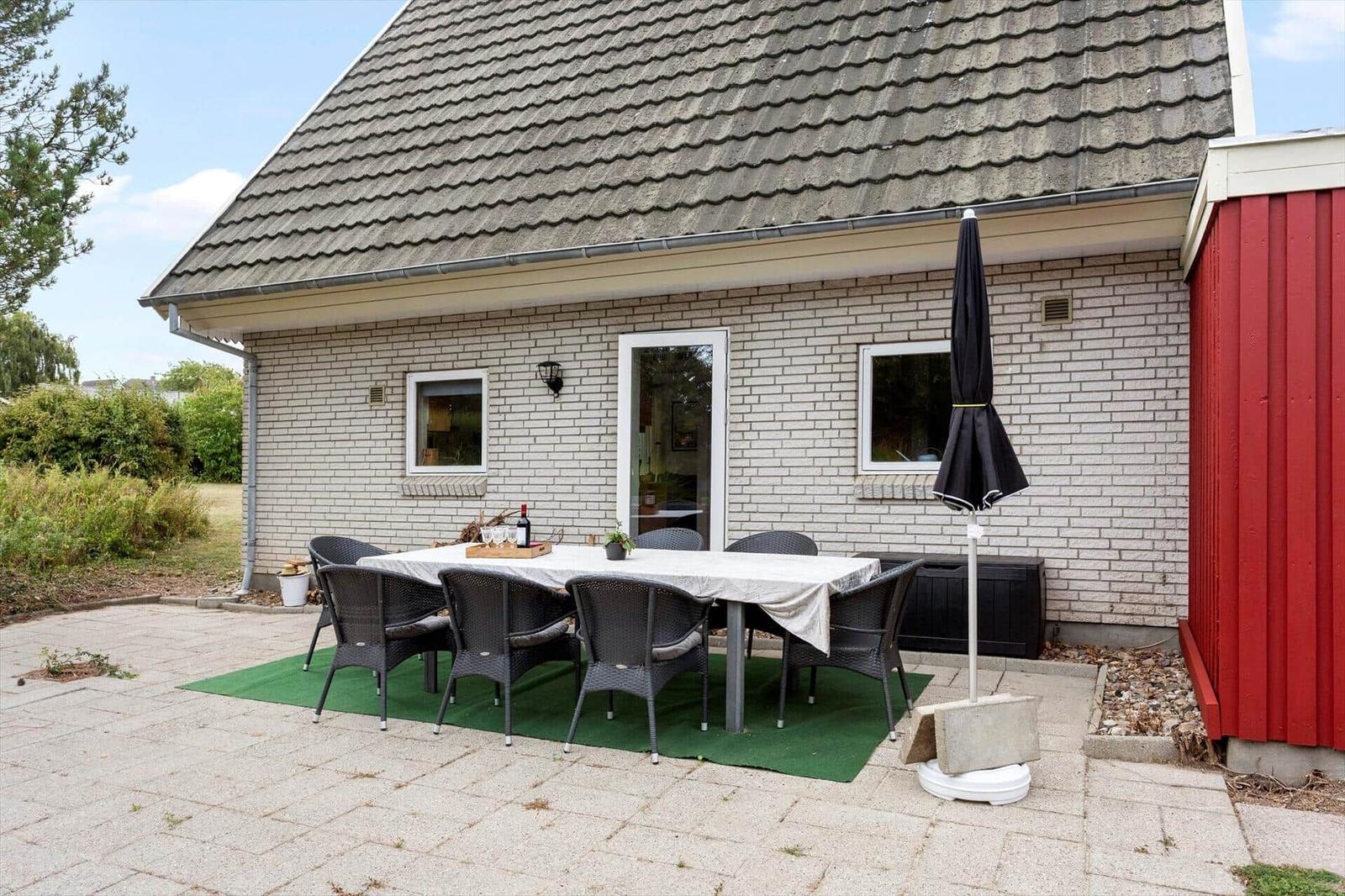 Terrace with table, white cloth, black chairs, green rug and brick wall.