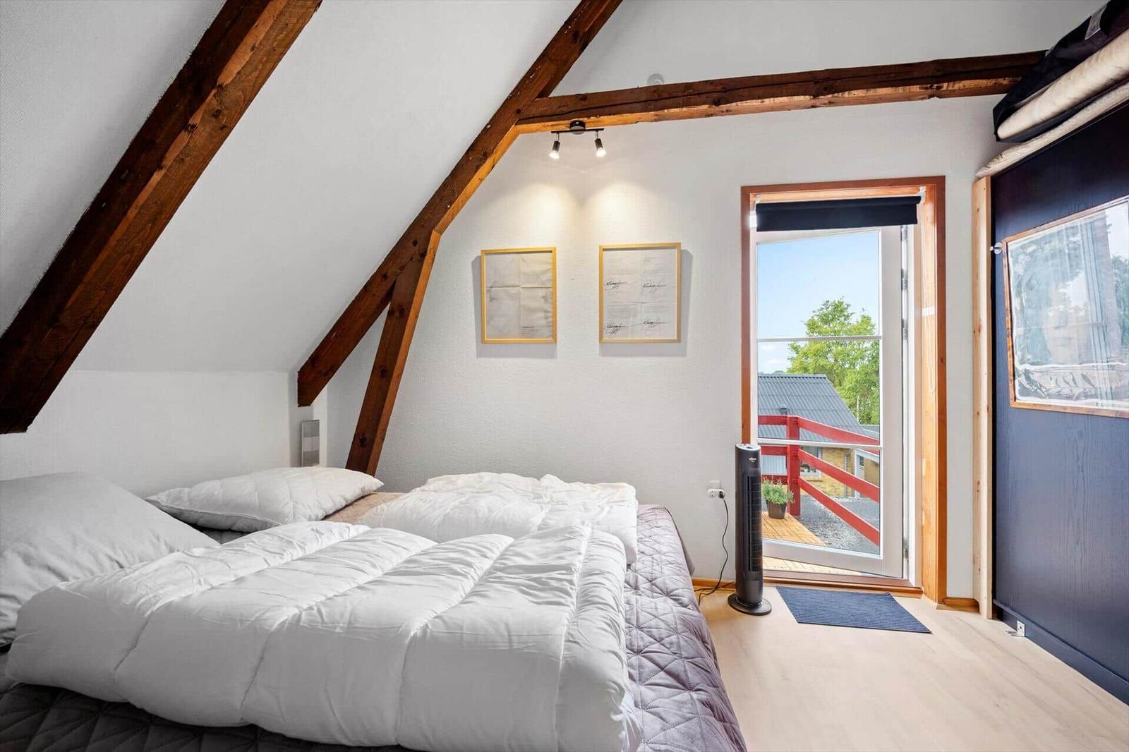 Attic bedroom with double bed, glass balcony door and exposed wooden beams.