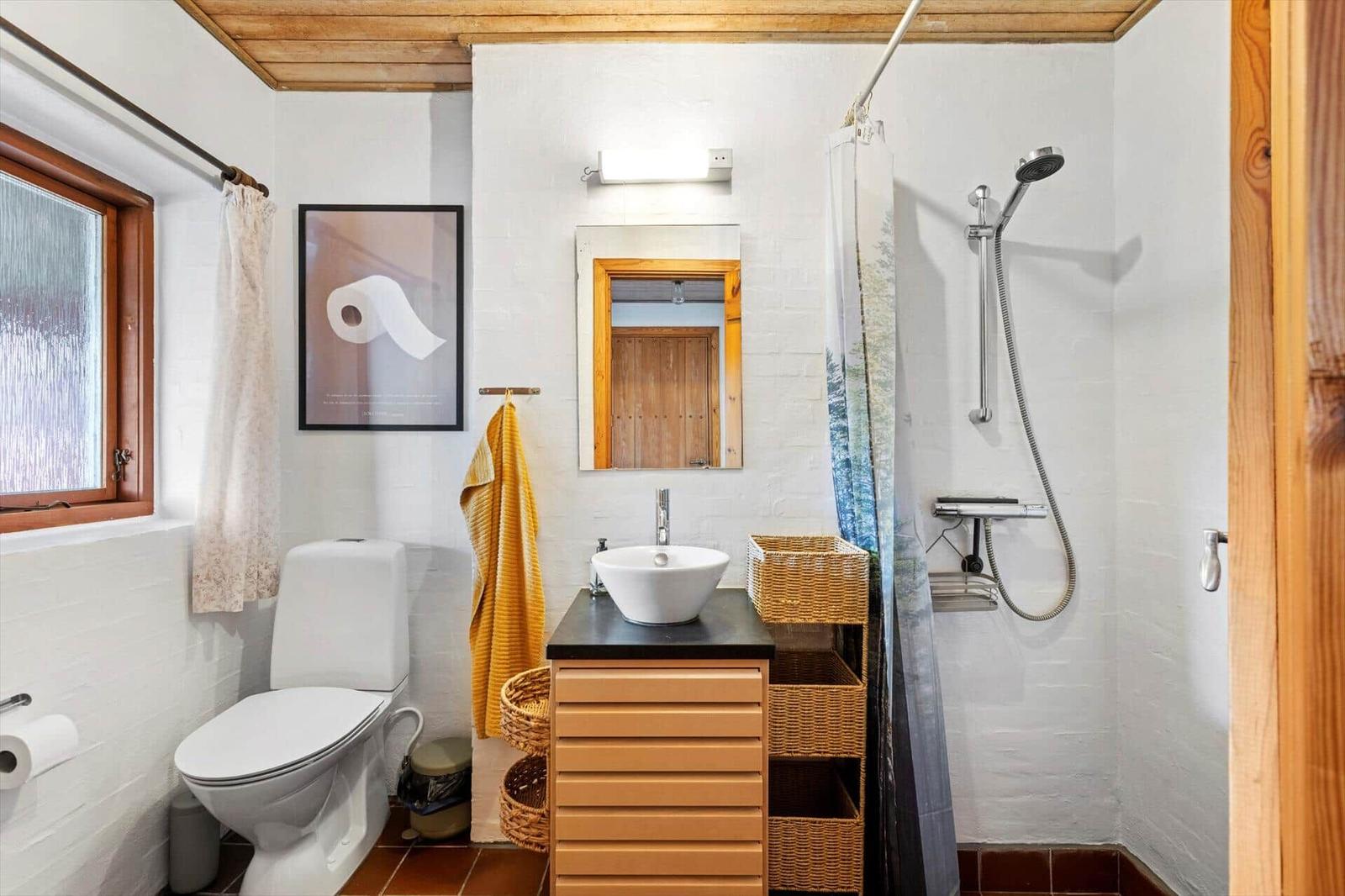 Bathroom with shower, toilet, vessel sink, wooden ceiling and wicker shelf.