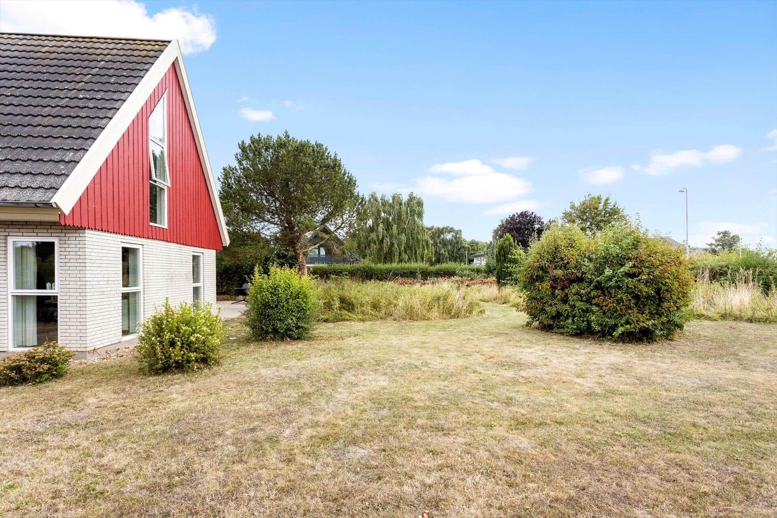 House with white ground floor, red wooden gable facade and garden lawn.