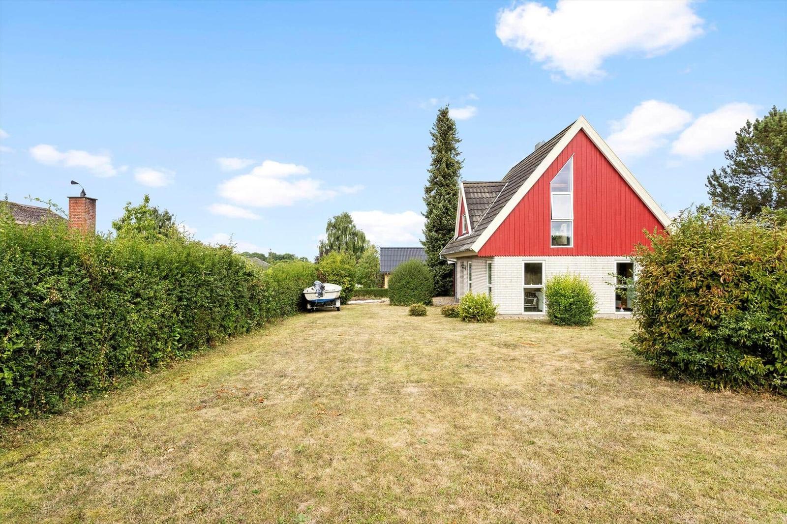 House with red wooden gable facade, white ground floor, large garden and motorboat.