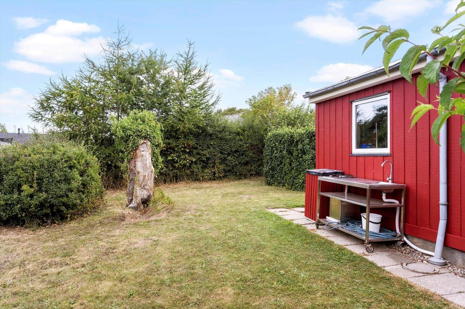 Stainless steel outdoor kitchen with sink by a red wooden wall and lawn.