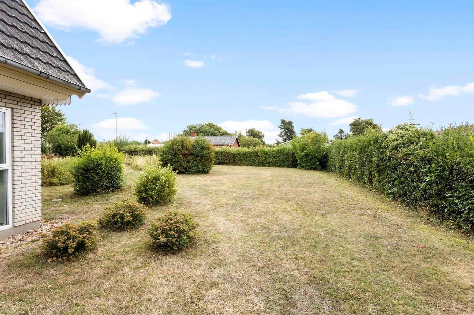 Garden with lawn area, tall hedges and bushes next to a light brick house.
