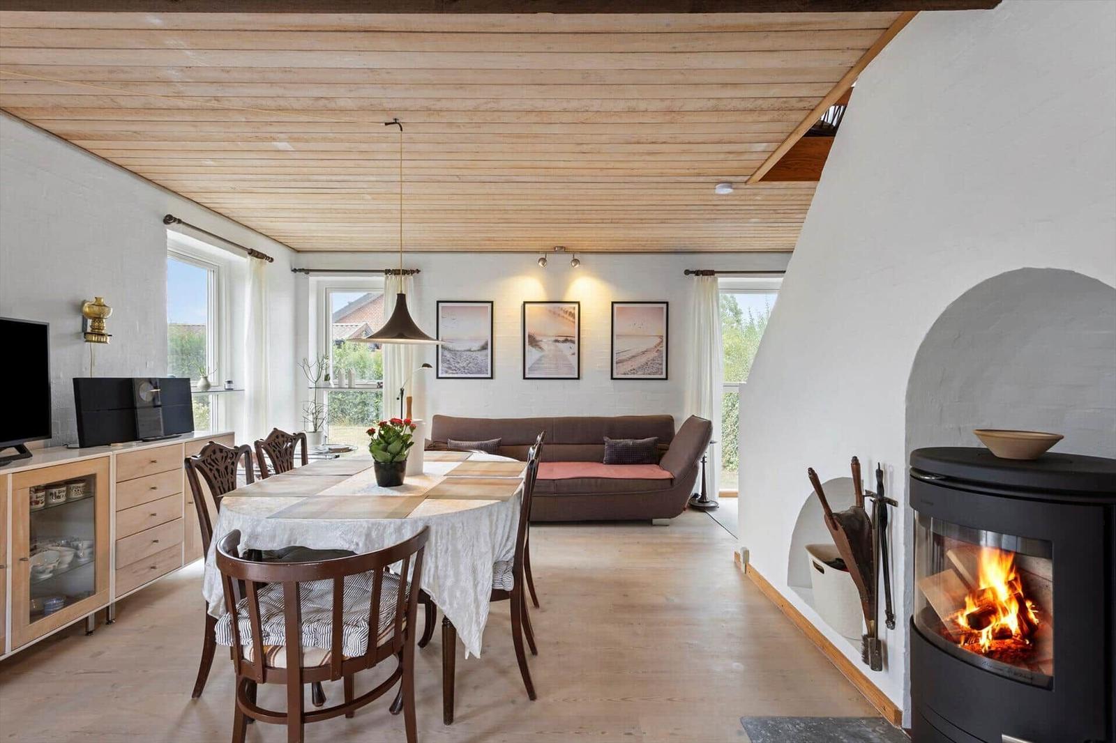 Dining area with round wooden table, chairs, wood stove, sofa and wooden ceiling.