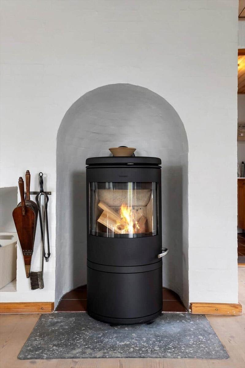 Black wood stove in a white arched alcove with fire and fireplace tools.