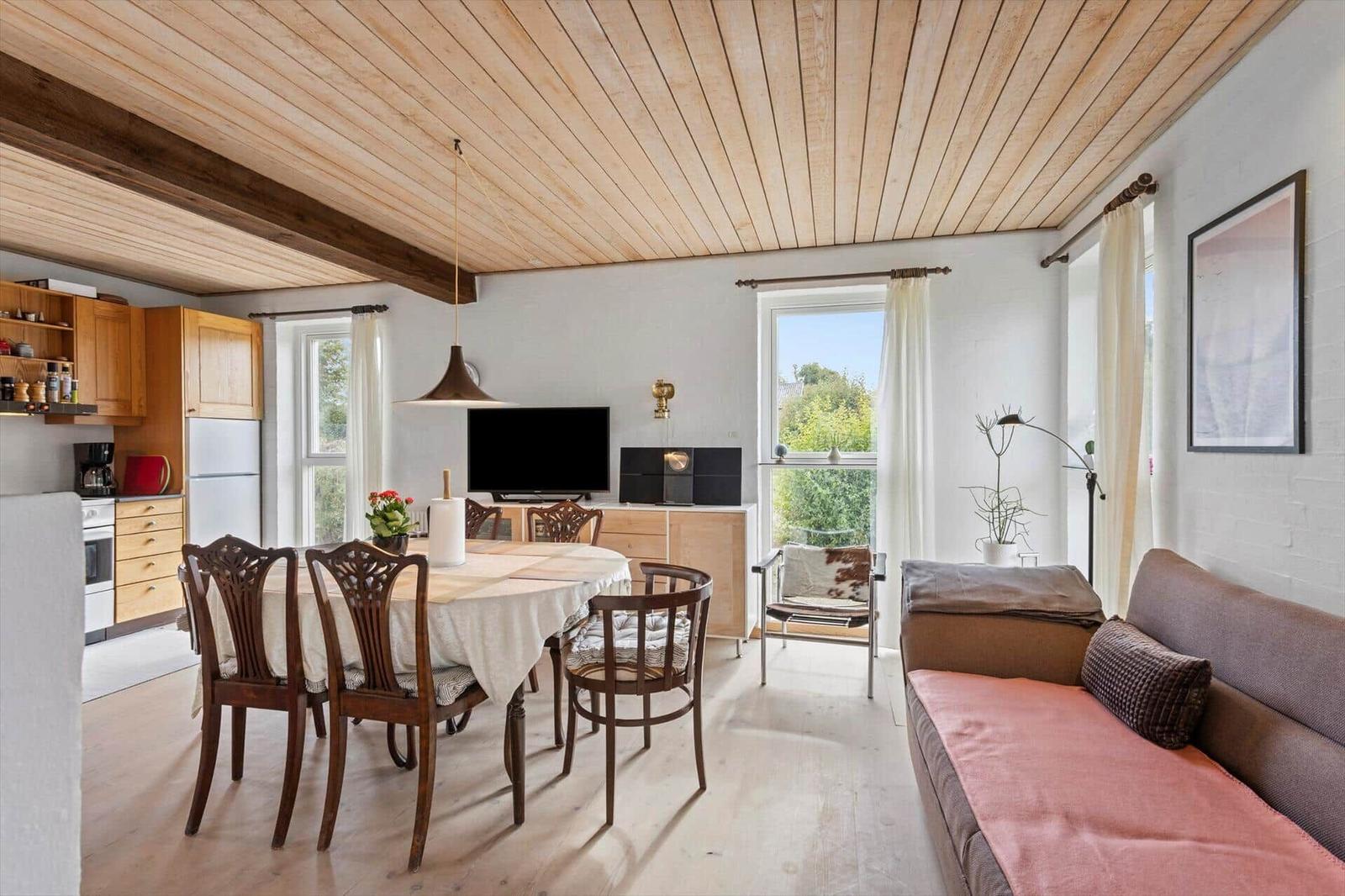 Living and dining room with table, sofa, TV board and open wooden kitchen.