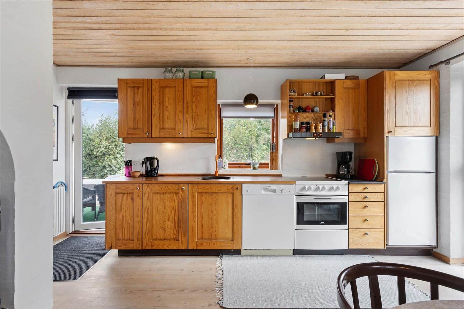 Wooden kitchen with white dishwasher, stove, fridge, window and terrace door.