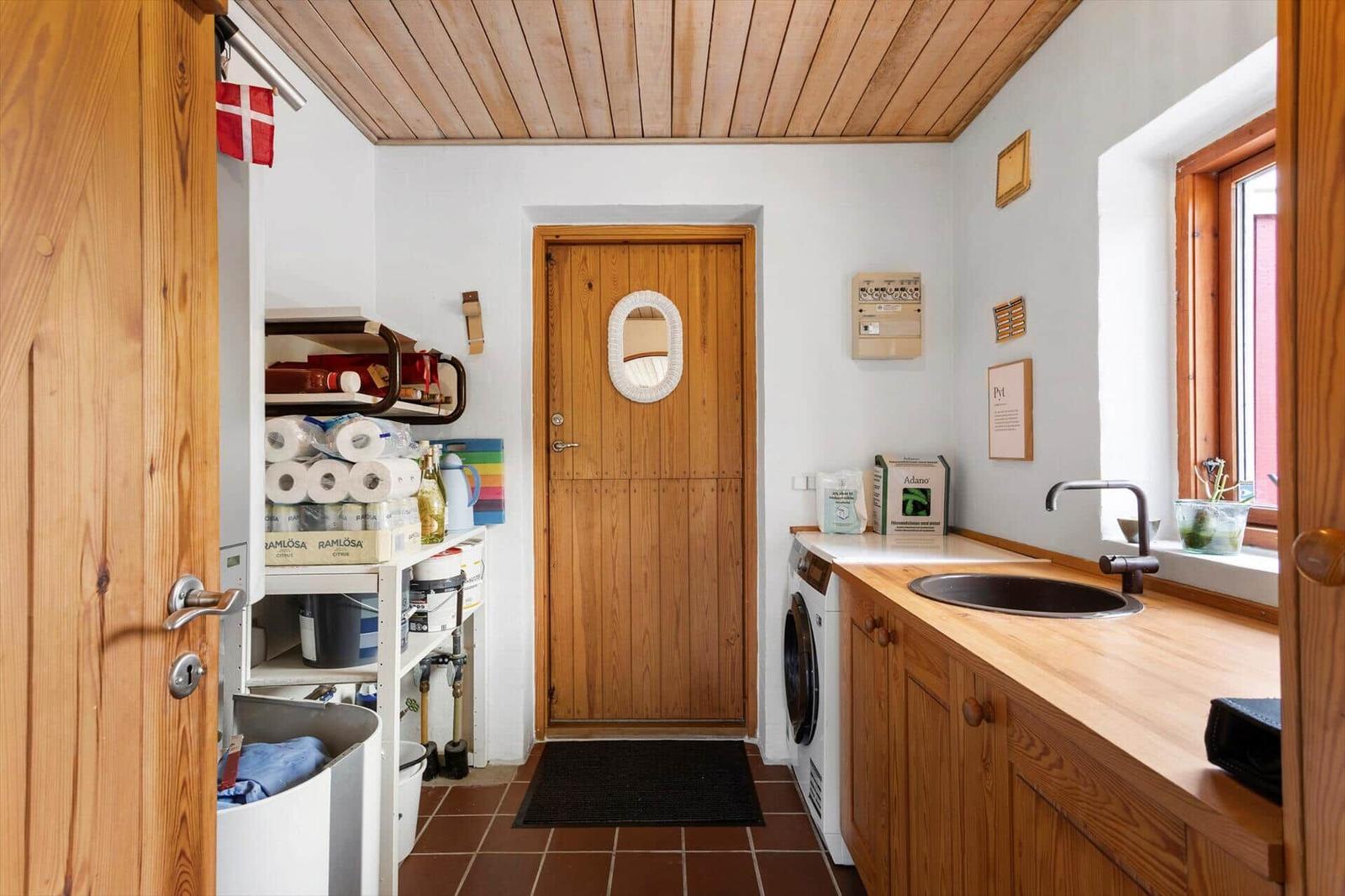 Utility room with washing machine, wooden counter, round sink and open shelf.