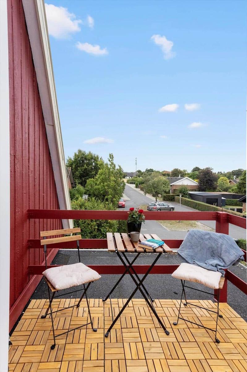 Balcony with wooden deck tiles, folding table, two chairs and view of the street.