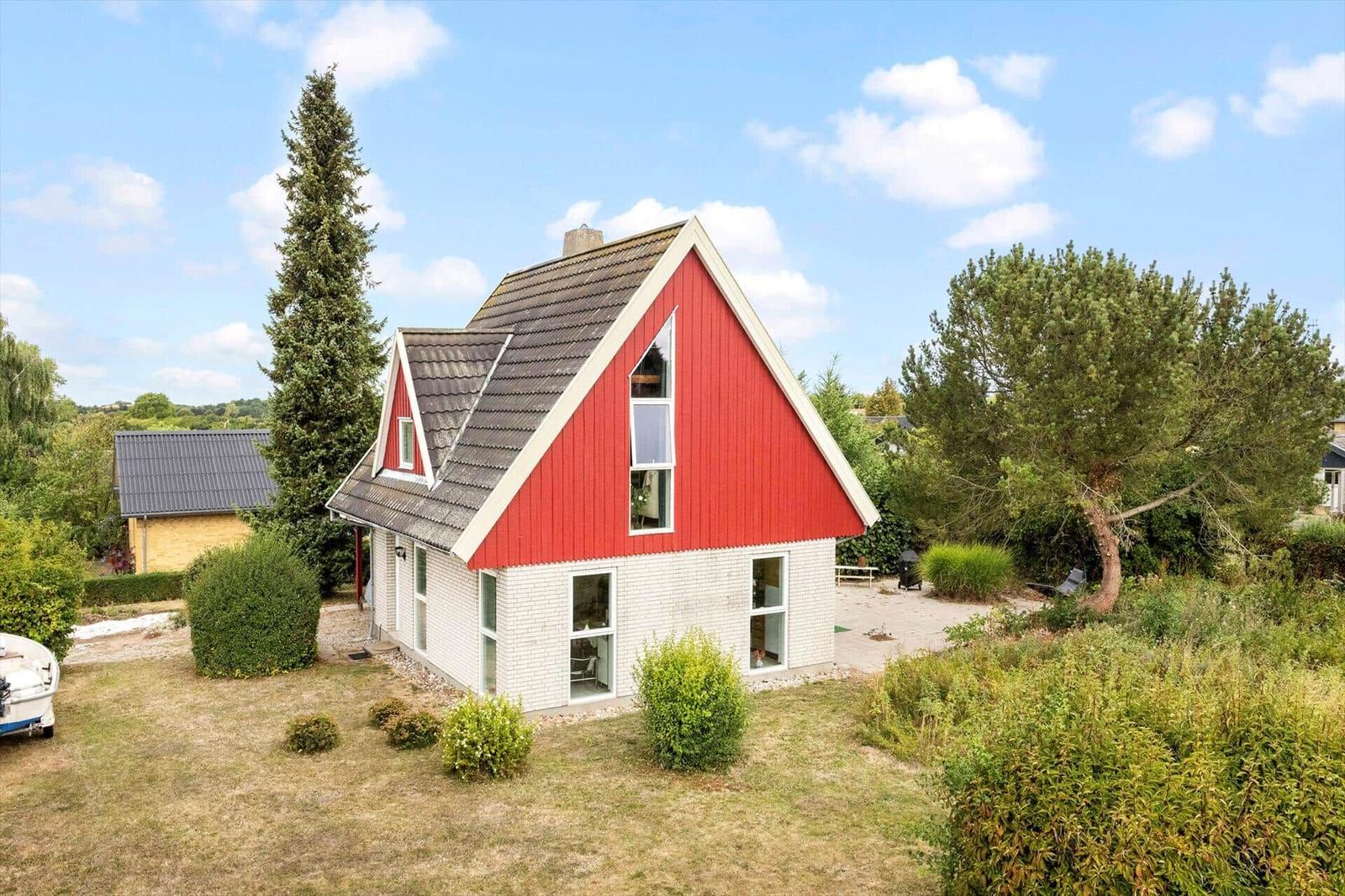 House with white brick facade, red wooden gable, dark roof and garden.