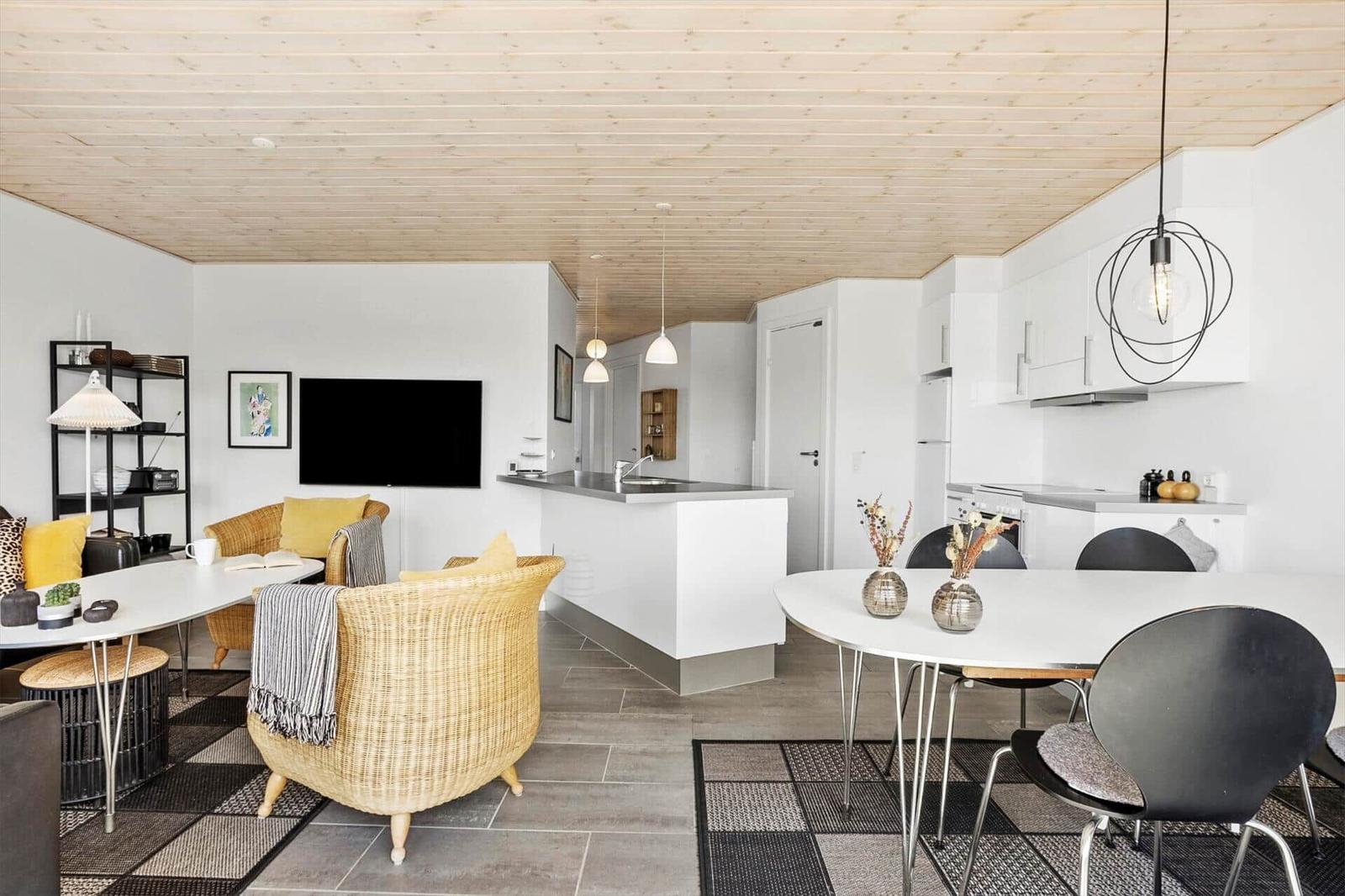Offenes Wohn-Esszimmer mit Korbsesseln, Esstisch, Kücheninsel und Holzdecke.