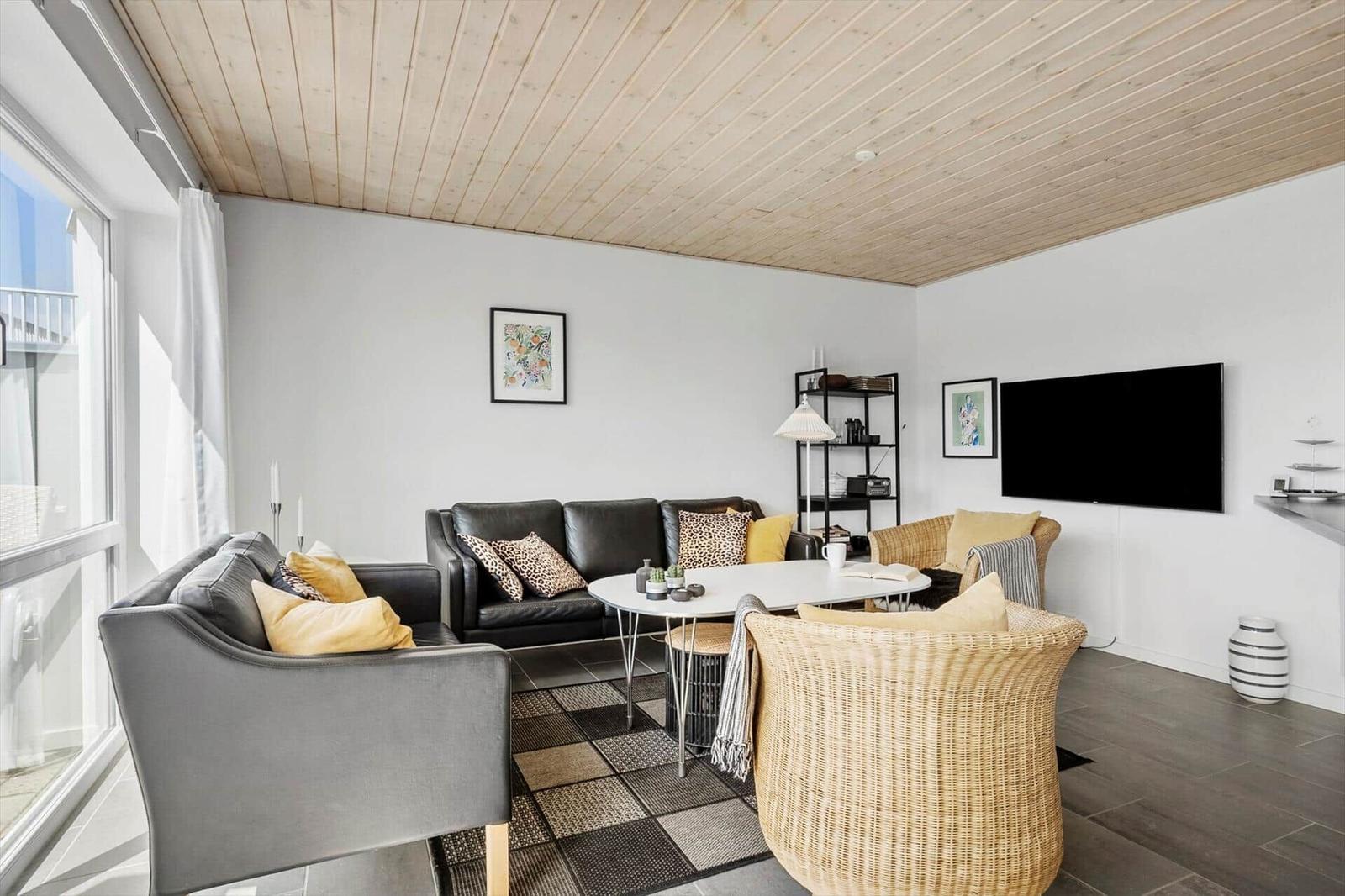 Wohnzimmer mit Ledersofas, Korbsesseln, Couchtisch, Fernseher und Holzdecke.