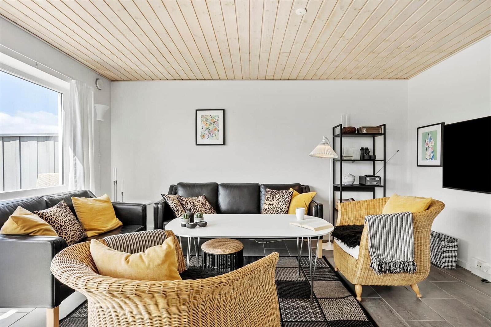 Wohnzimmer mit schwarzen Sofas, Korbsesseln, kariertem Teppich und Stehlampe.
