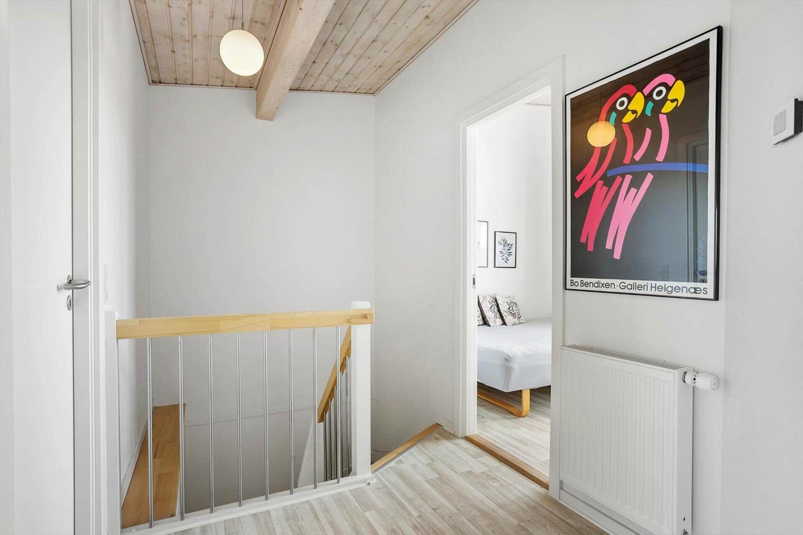 Flur im Obergeschoss mit Treppengeländer, Holzdecke und Blick ins Schlafzimmer.