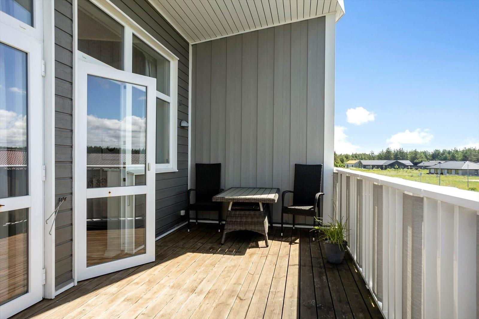 Holzbalkon mit Rattanstühlen, Tisch, weißem Geländer und Blick auf Häuser.