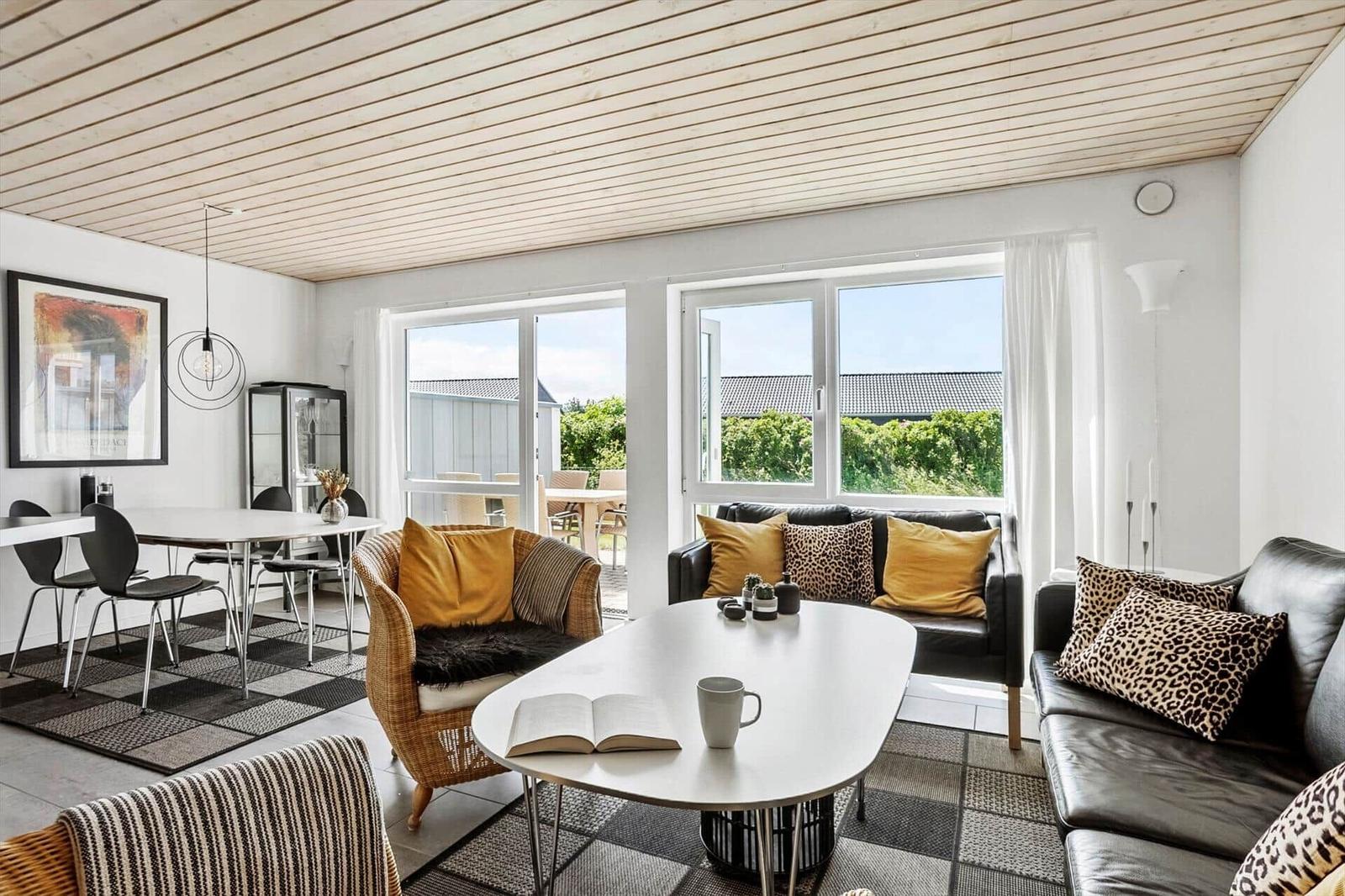 Wohnzimmer mit schwarzem Sofa, Korbsessel, Couchtisch, Teppichen und Essbereich.