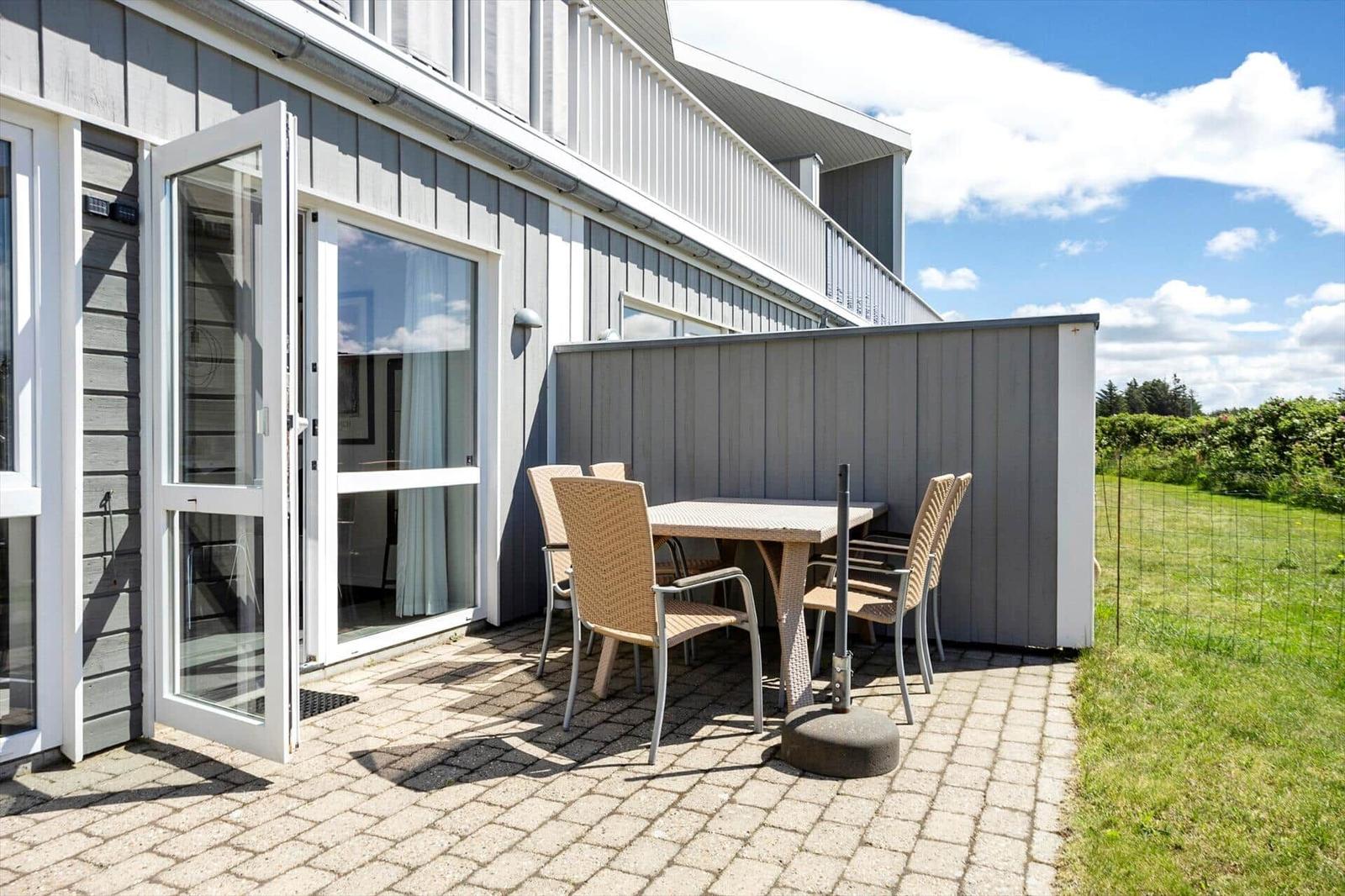 Terrasse mit Rattantisch, vier Stühlen, Pflaster und grauer Holzfassade.