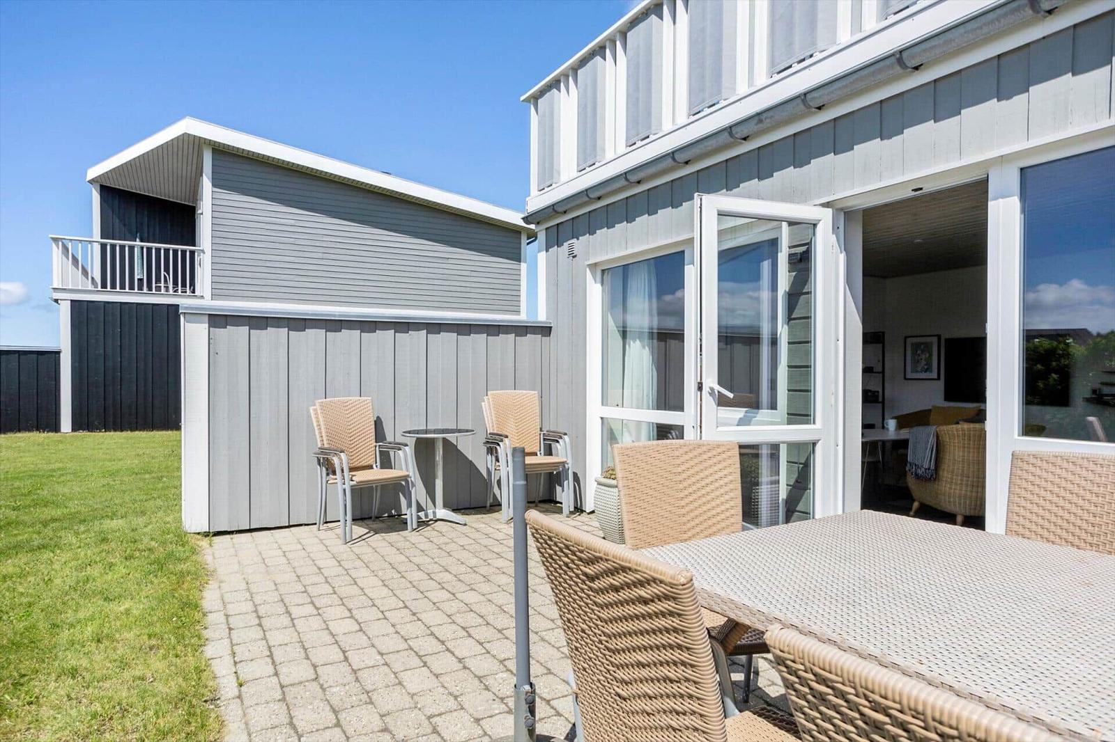 Terrasse mit Rattansesseln, Tischgruppen, Pflaster und Rasen vor dem Haus.