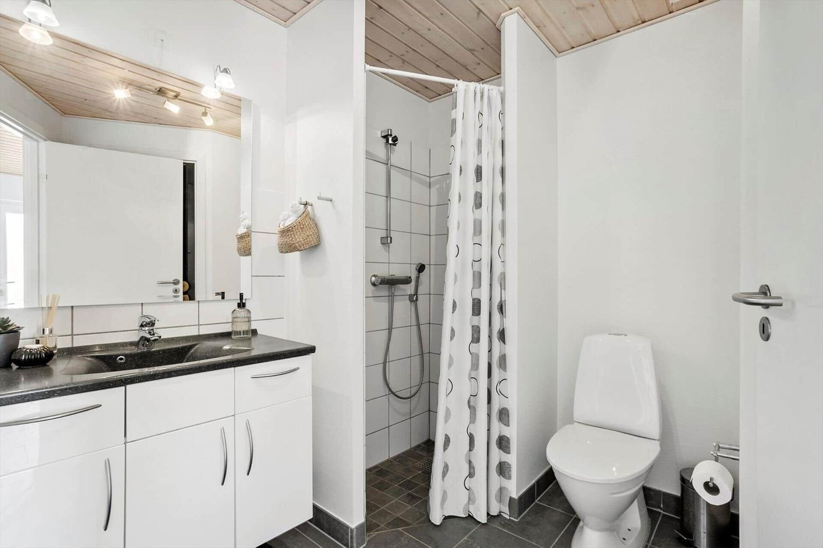Badezimmer mit dunklem Waschtisch, Dusche mit Vorhang, WC und Holzdecke.