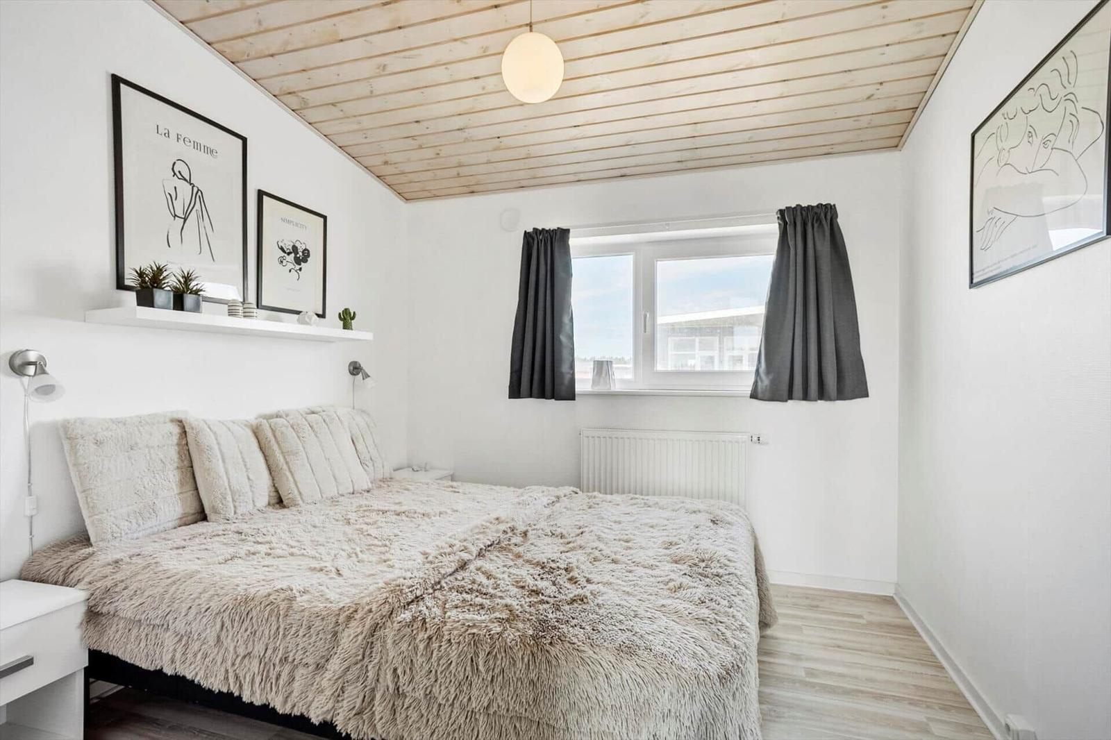 Schlafzimmer mit flauschiger Bettwäsche, Holzdecke, Kugellampe und Fenster.