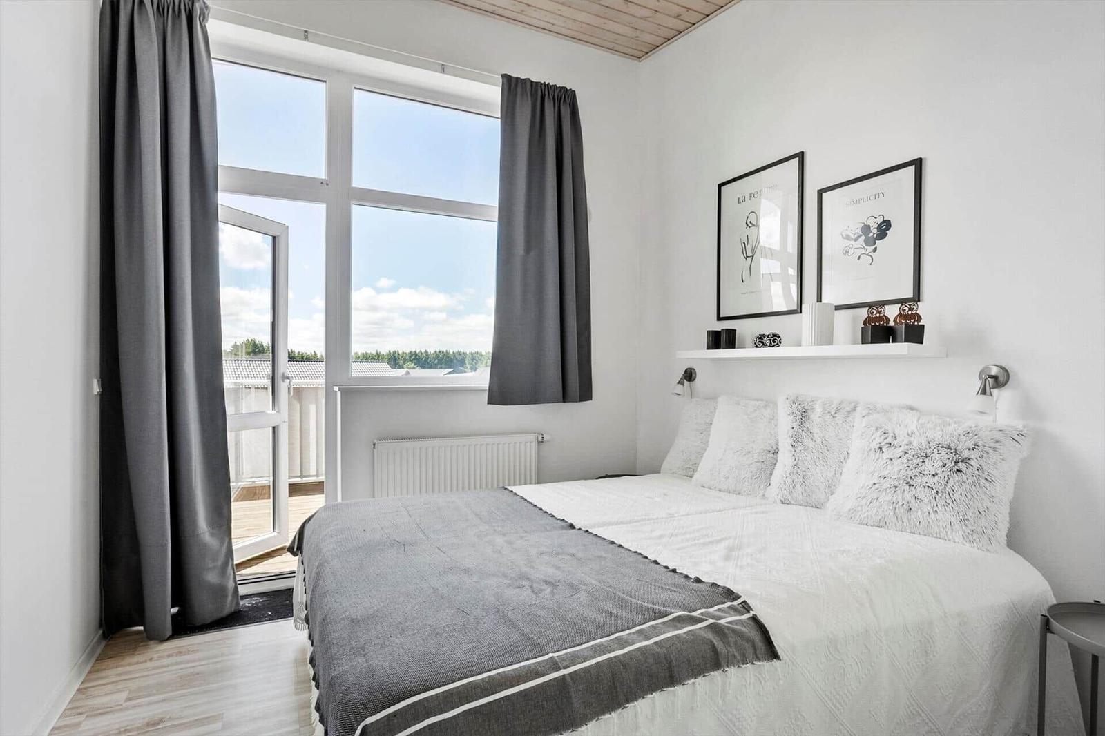 Schlafzimmer mit Doppelbett, grauen Vorhängen, Balkonzugang und Wandlampen.