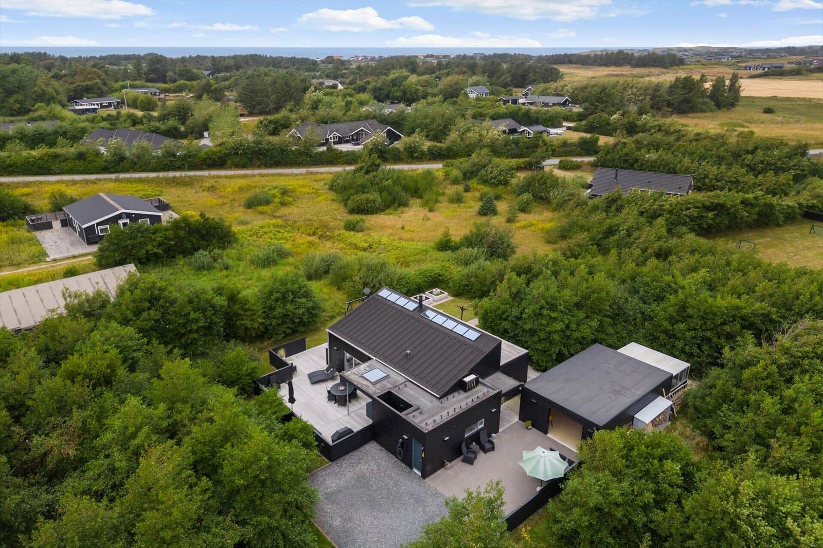 Aerial view of a black wooden house with terrace, trees and nearby houses.