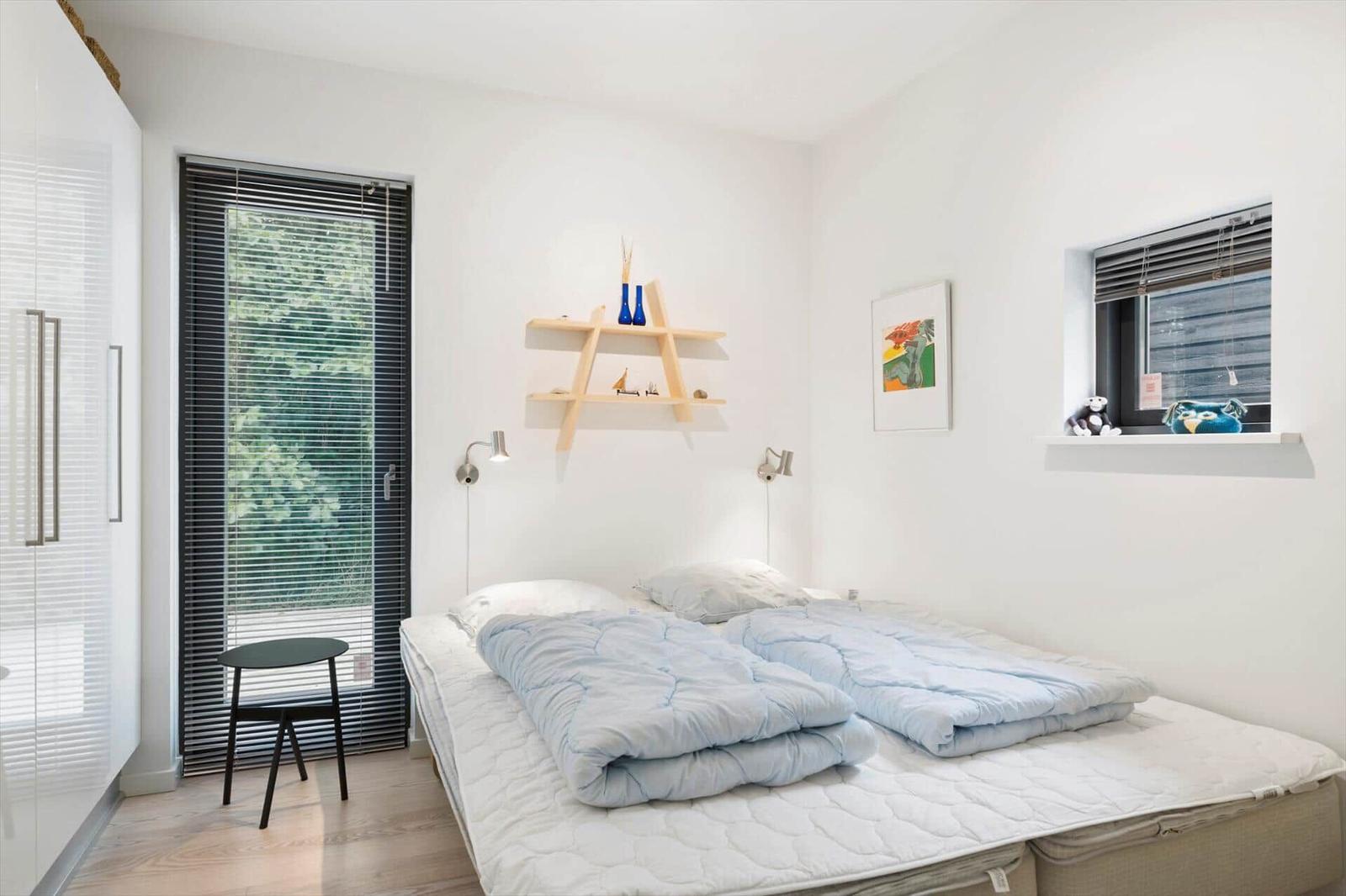 Bedroom with double bed, blue duvets, wall shelf and windows with blinds.