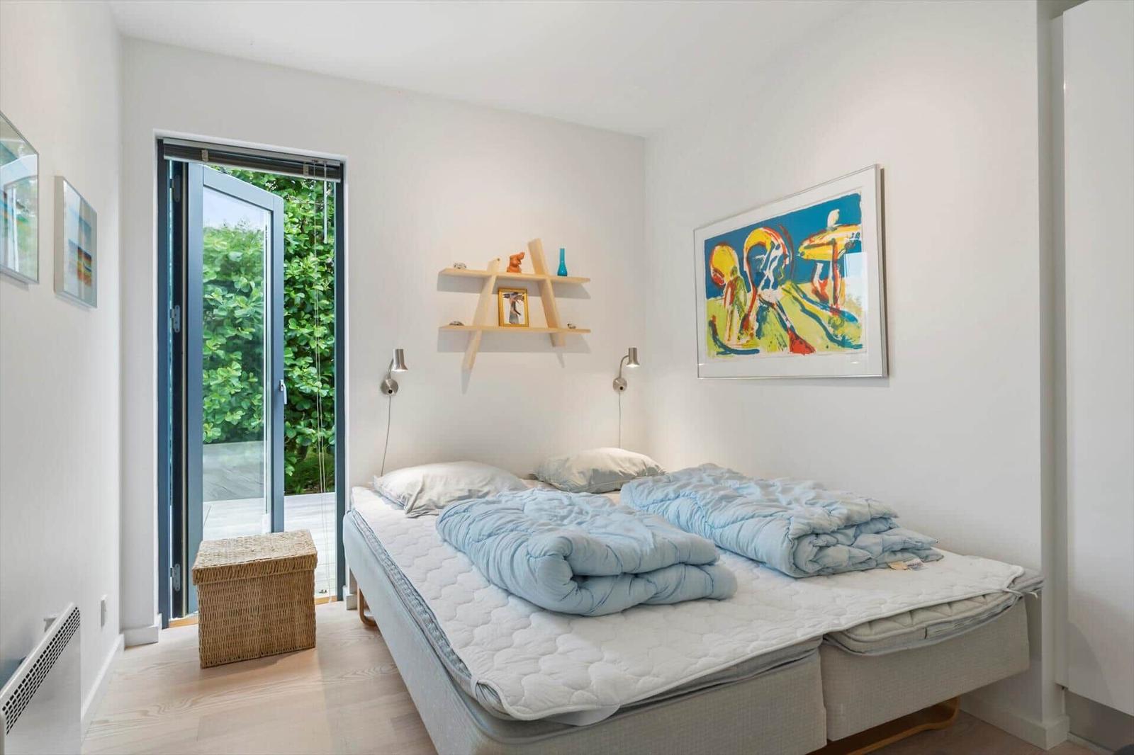 Bedroom with double bed, colourful wall painting and an open terrace door.