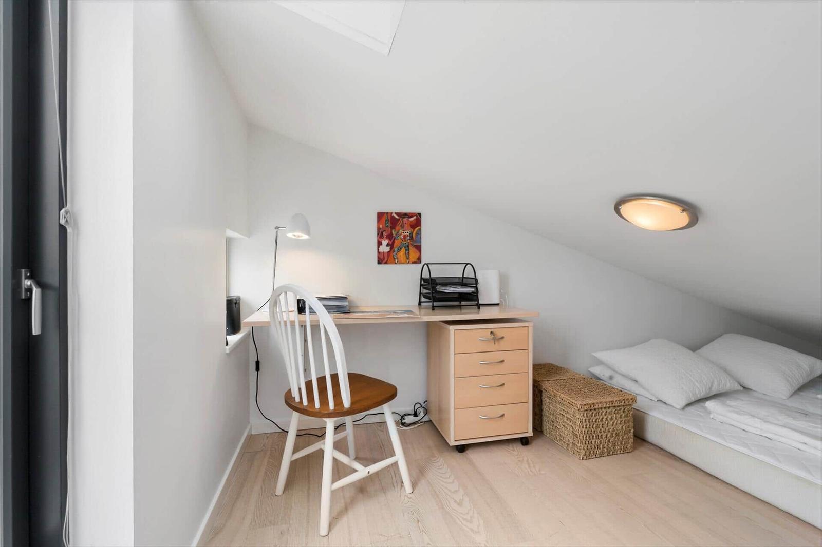 Attic room with desk, chair and a mattress under the sloped ceiling.