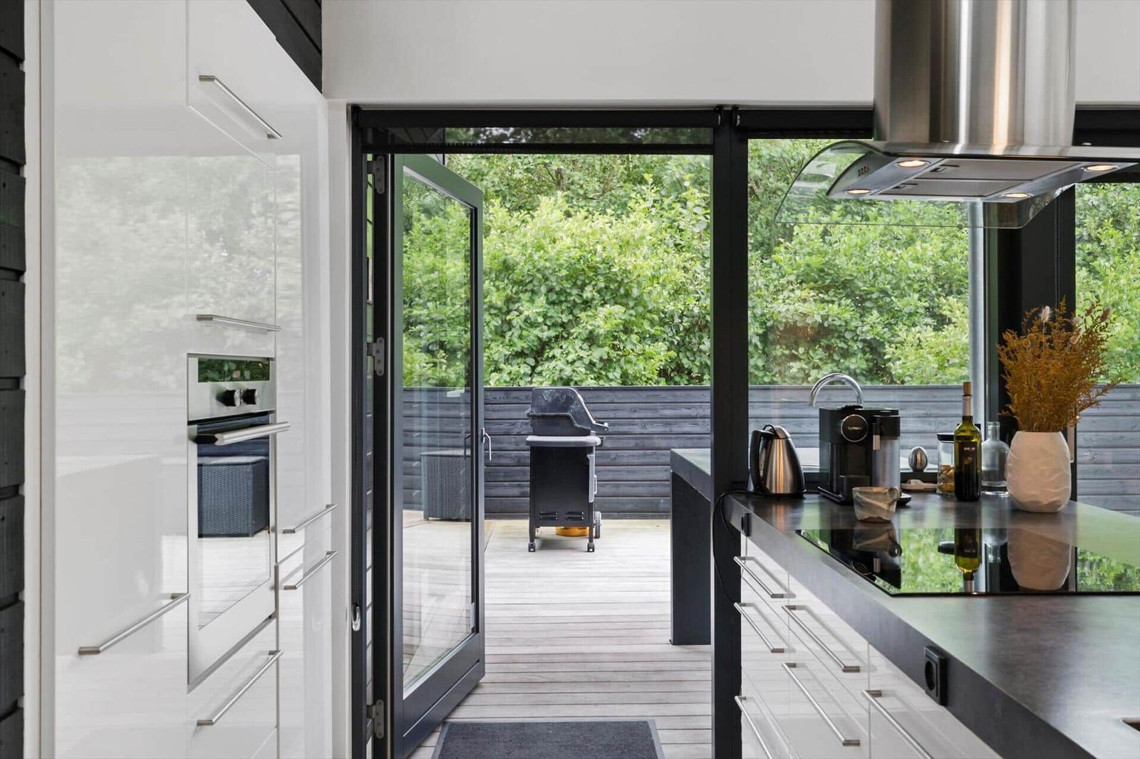 White kitchen with hob, extractor hood and open door to terrace with grill.