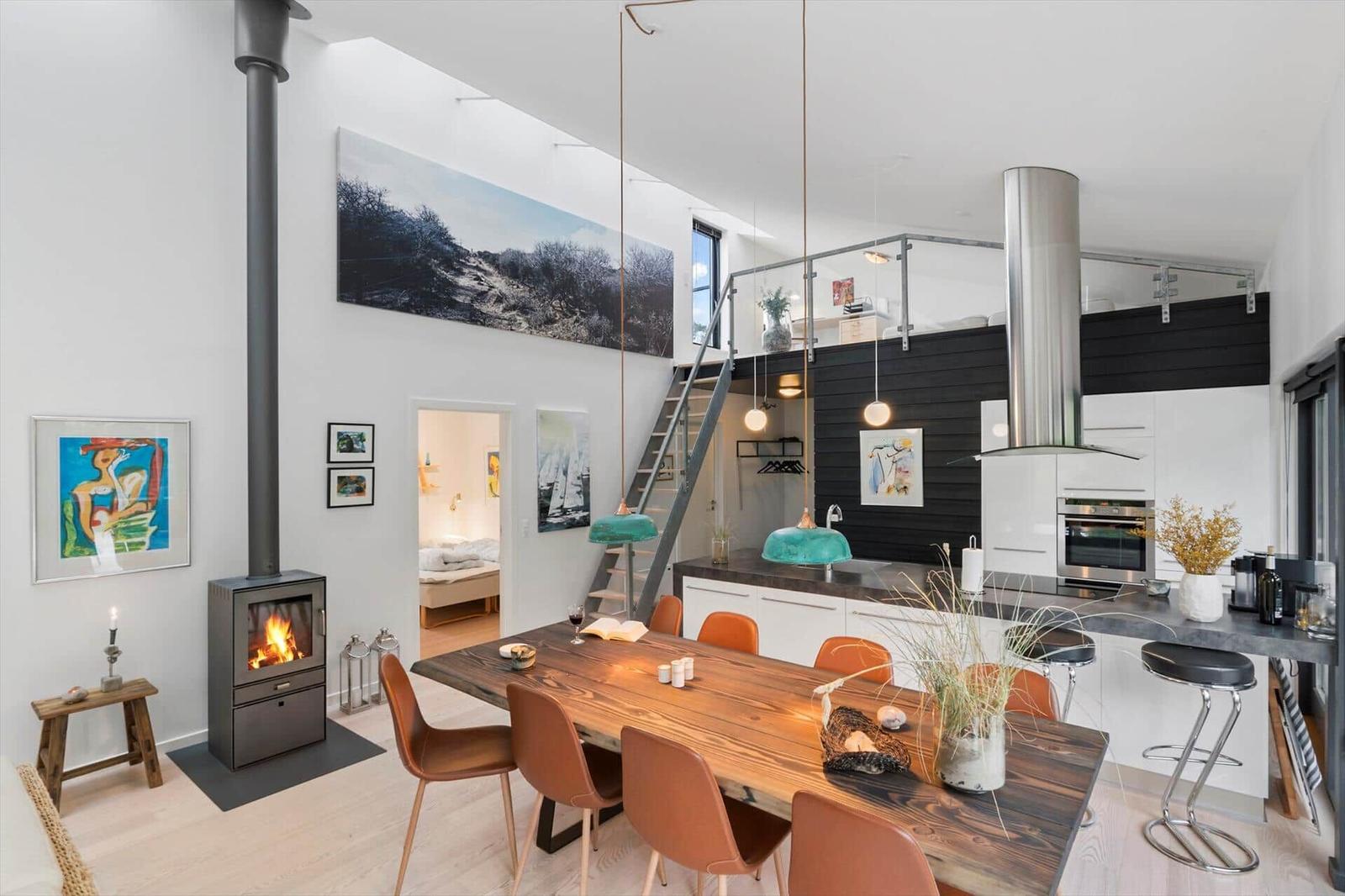 Open living space with dining table, kitchen, wood stove and stairs to a loft.