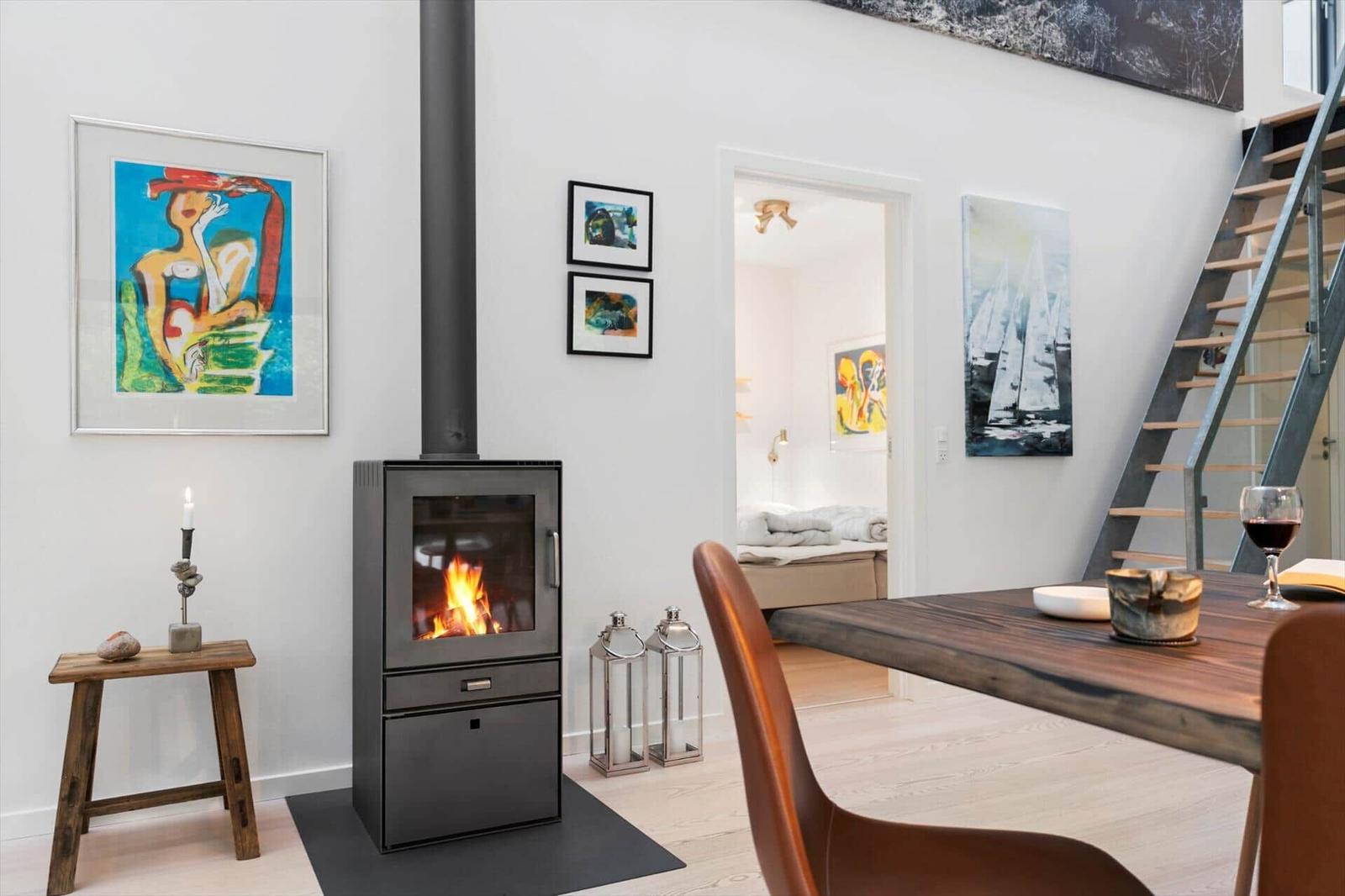 Black wood stove with fire, dining table, stairs and view into a bedroom.