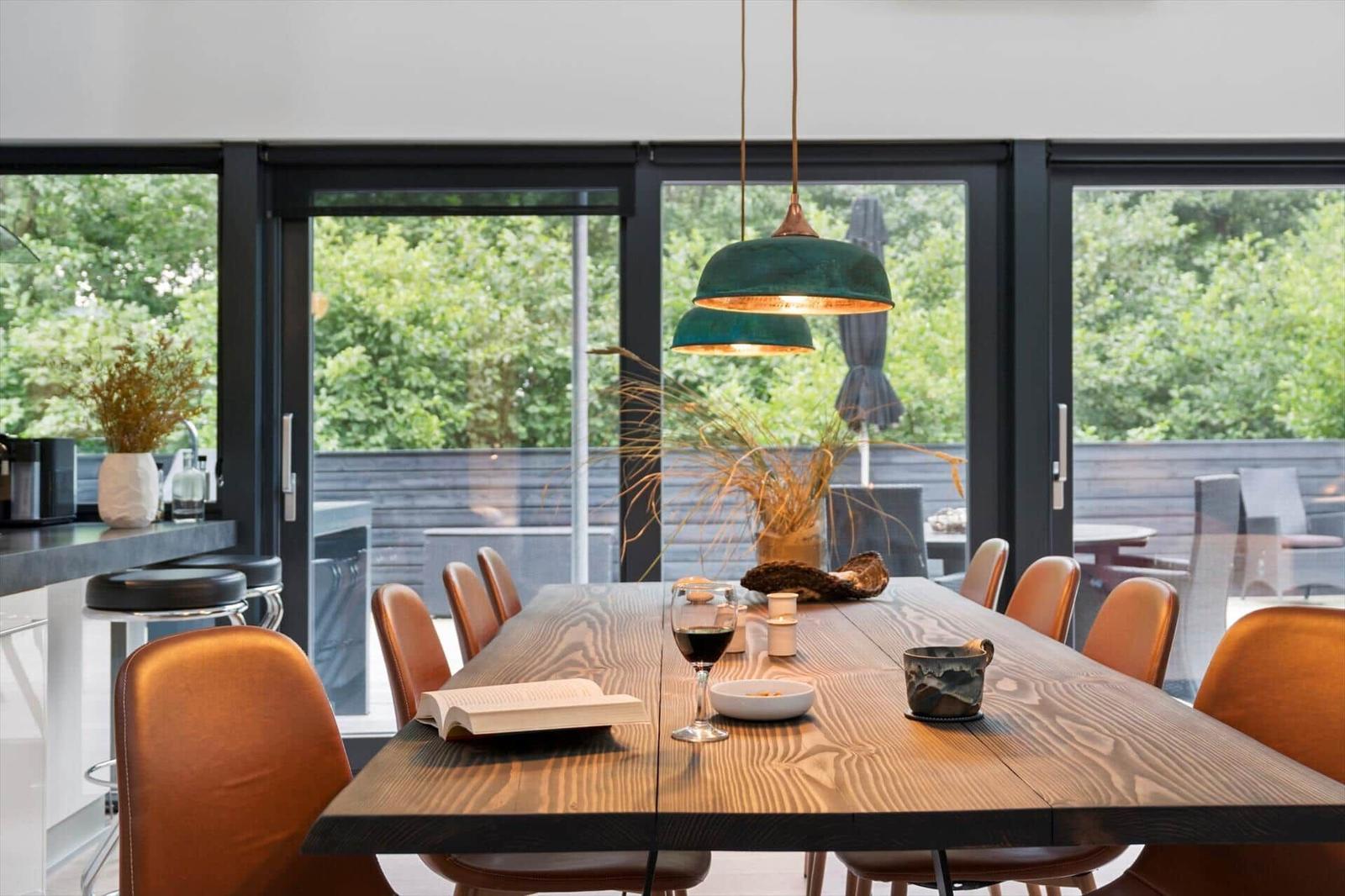 Long wooden table with brown chairs, pendant lamps and glass doors to the terrace.