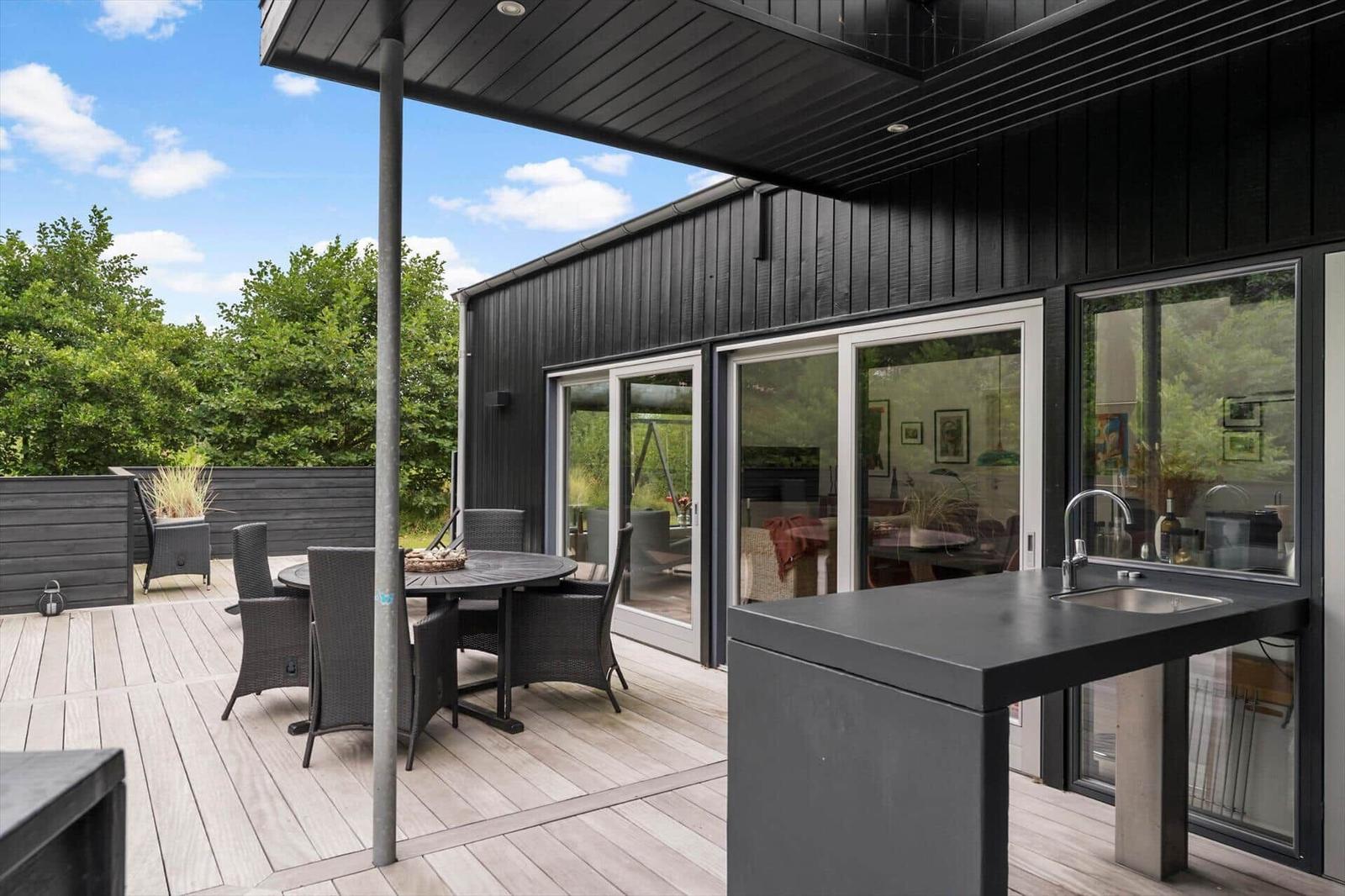 Wooden terrace with round table, wicker chairs and outdoor sink by glass doors.