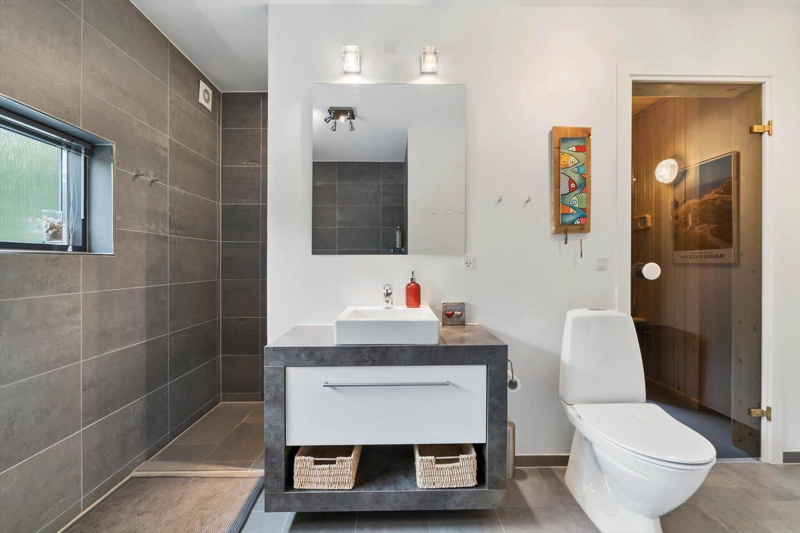 Bathroom with dark vanity, white sink, large mirror, walk-in shower and toilet.