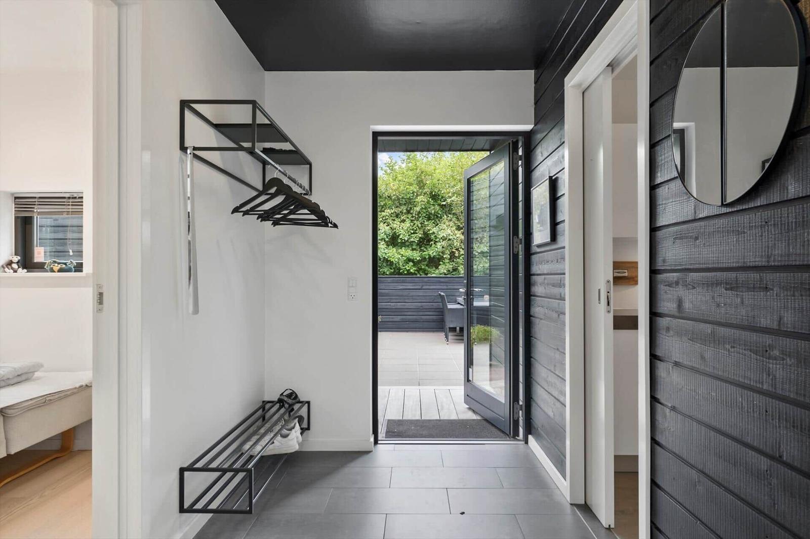 Hallway with black wood cladding, round mirror, coat rack and terrace door.